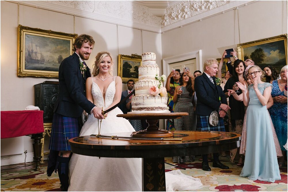  A young married couple cutting into their spectacular wedding cake with a sword at a Summer wedding at Winton castle Scotland  