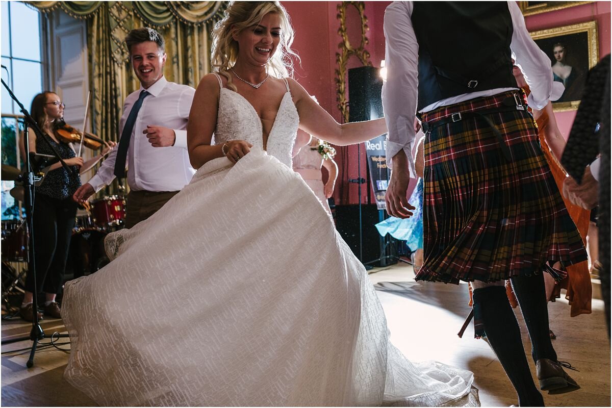  A bride in a white dress during a ceilidth at a Summer wedding at Winton castle Scotland with rustic flowers and bride speech 
