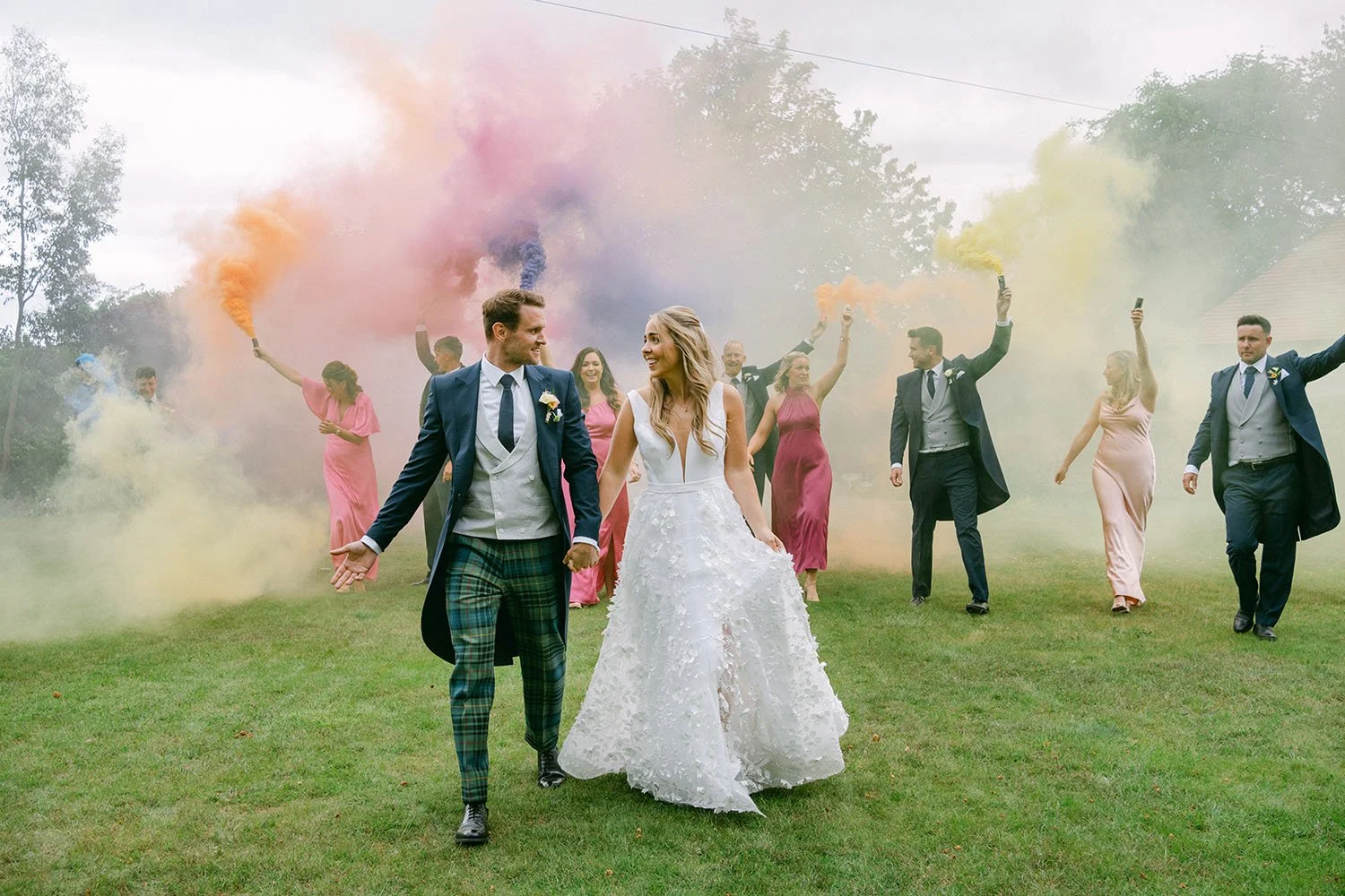 A wedding party with bridesmaid & groomsmen walking with coloured smoke bombs in East Lothian, near Edinburgh, Scotland 