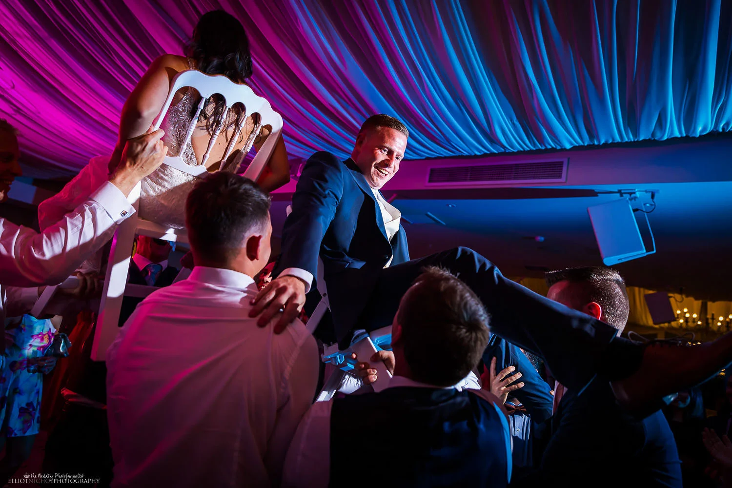 Bride and groom are lifted in their seats in the air during their wedding reception party. Photo by Elliot Nichol Photography.