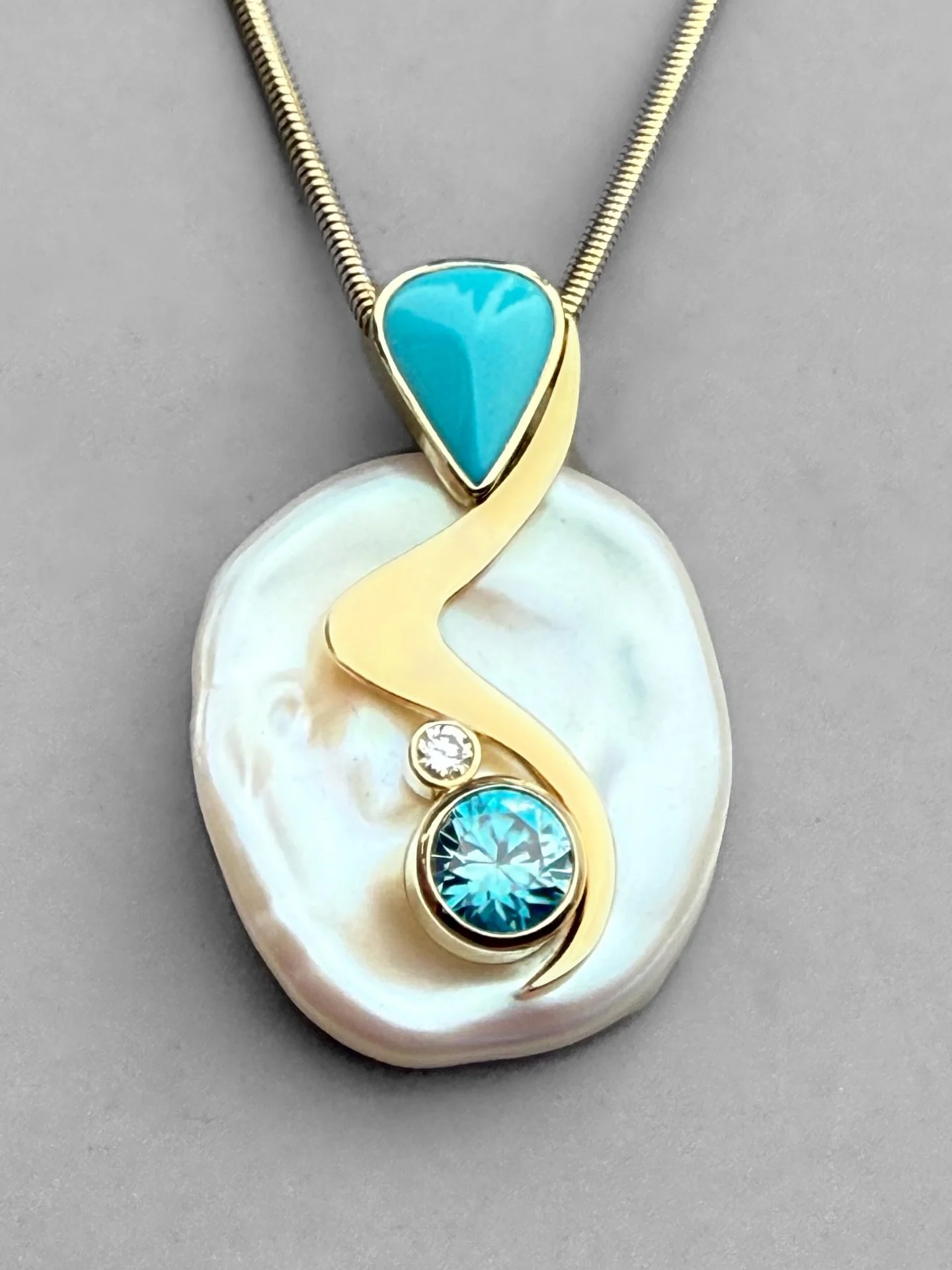 This beautiful pendant, designed by Jan Daggett, covers two of December&rsquo;s birthstones. With a sweet sleeping beauty turquoise accent and the large, vibrant, blue zircon, this pearl piece is truly one of a kind. Found here in the gallery, and so