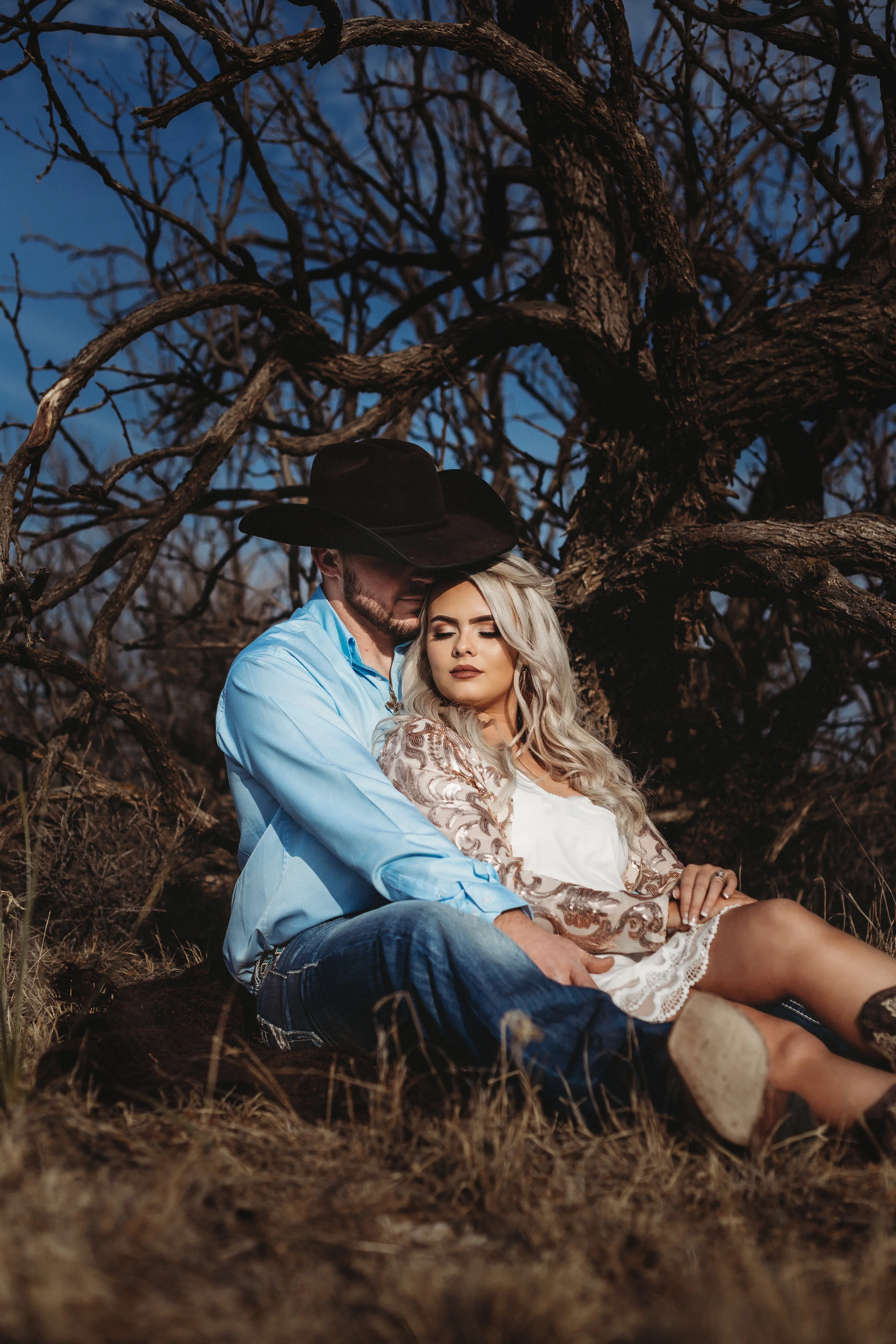 Close up of engaged couple sitting with dark bare trees behind them #engagementphotos #engaged #personality #amarillotexas #engagementphotographer #lifestylephotos #amarillophotographer #locationchoice #texasengagementphotos #engagment #tealawardphotography #westernstyle