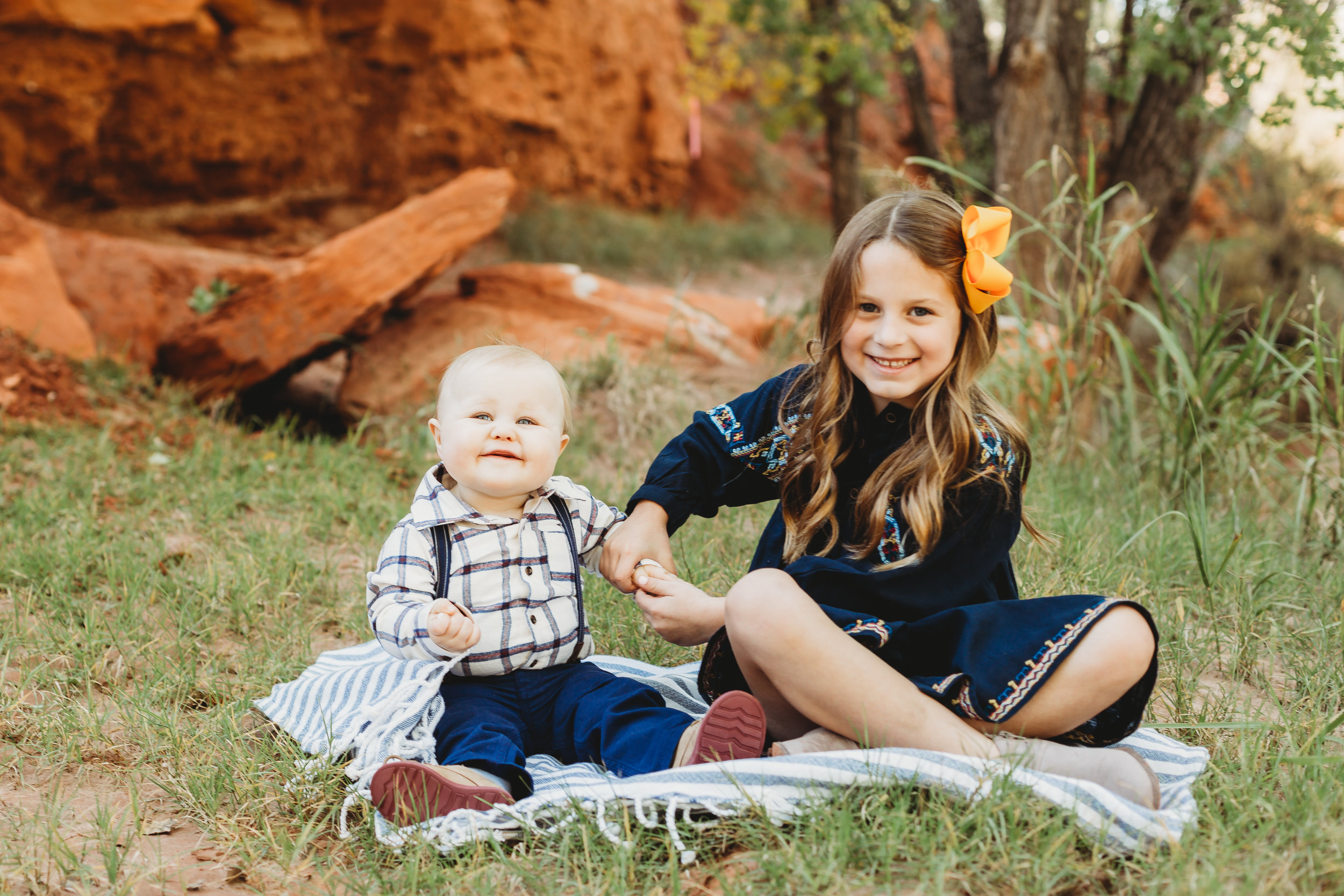 Brother and sister sitting on picnic blanket with greenery and red rock behind them smiling at the camera #tealawardphotography #texasfamilyphotographer #amarillophotographer #amarillofamilyphotographer #lifestylephotography #emotionalphotography #familyphotosoot #family #lovingsiblings #purejoy #familyphotos #familyphotographer #greatoutdoors
