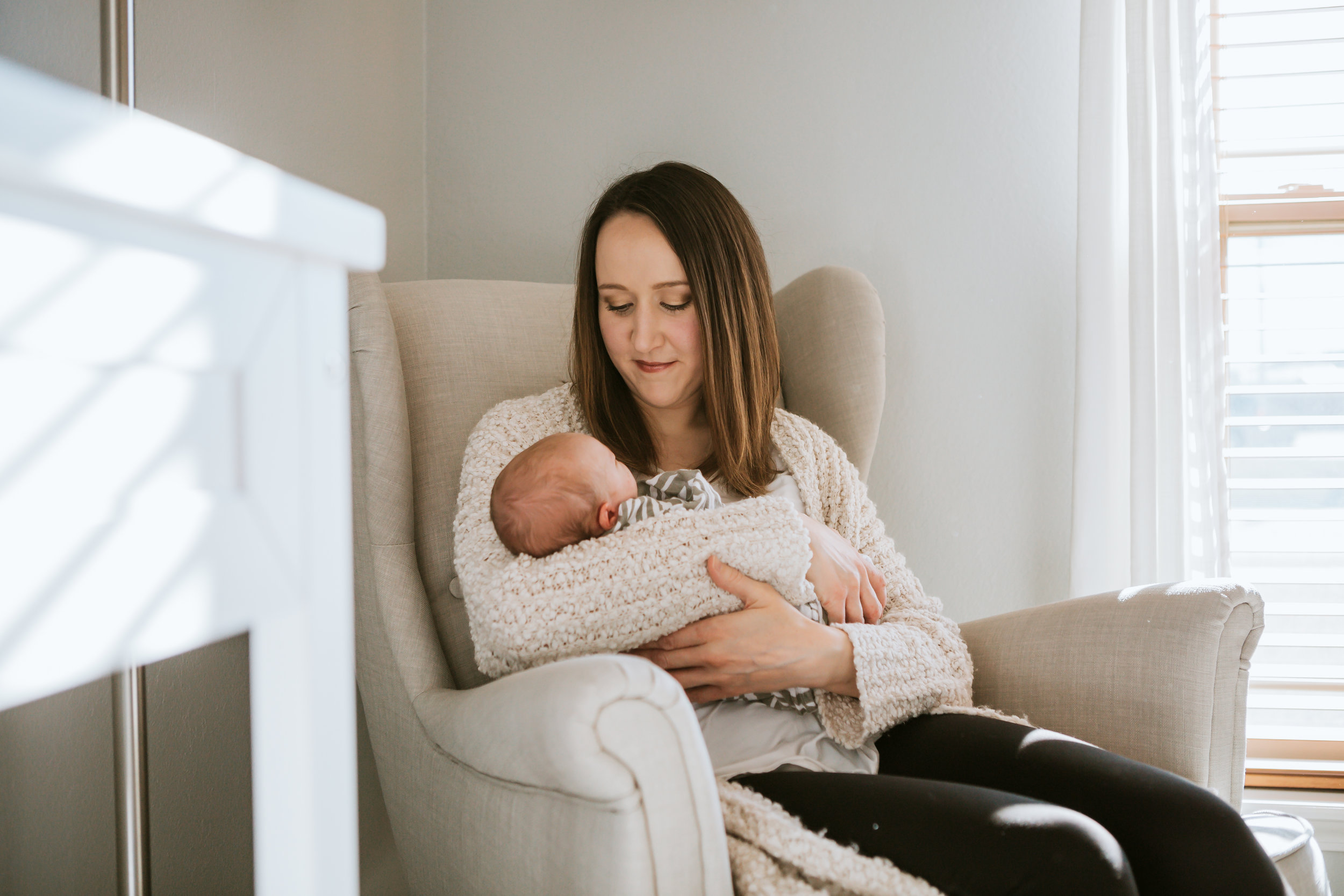  Mom holding her new little one in their nursery chair in neutral colors #tealawardphotography #texasnewbornphotographysession #amarillophotographer #amarilloenewbornphotographer #emotionalphotography #lifestylephotography #inhomesession #lifestyles #newbaby #newfamilyofthree #sweetbaby #nurseryphotos 