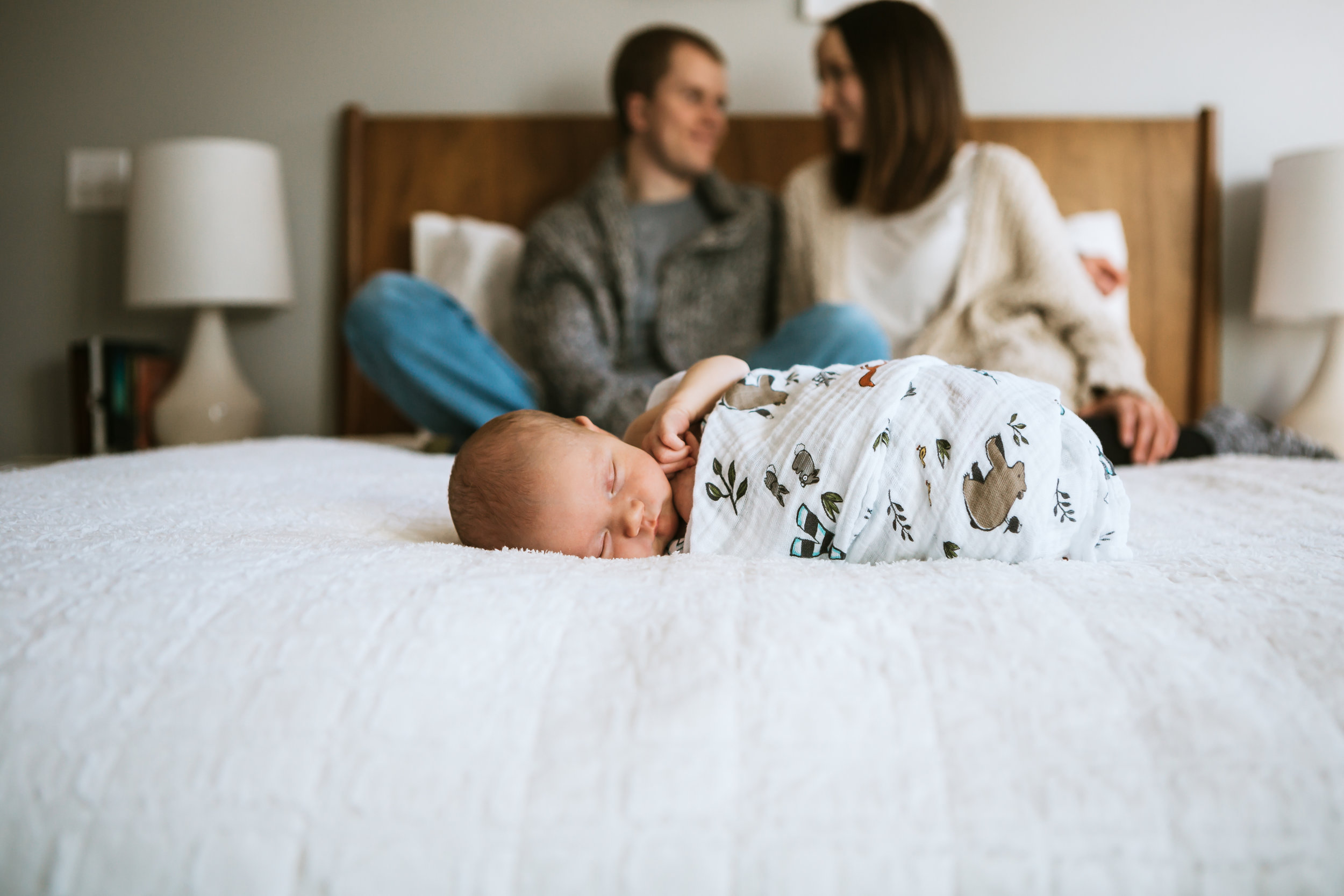  Close up of baby on the bed with mom and dad sitting on the bed behind him #tealawardphotography #texasnewbornphotographysession #amarillophotographer #amarilloenewbornphotographer #emotionalphotography #lifestylephotography #inhomesession #lifestyles #newbaby #newfamilyofthree #sweetbaby #nurseryphotos 
