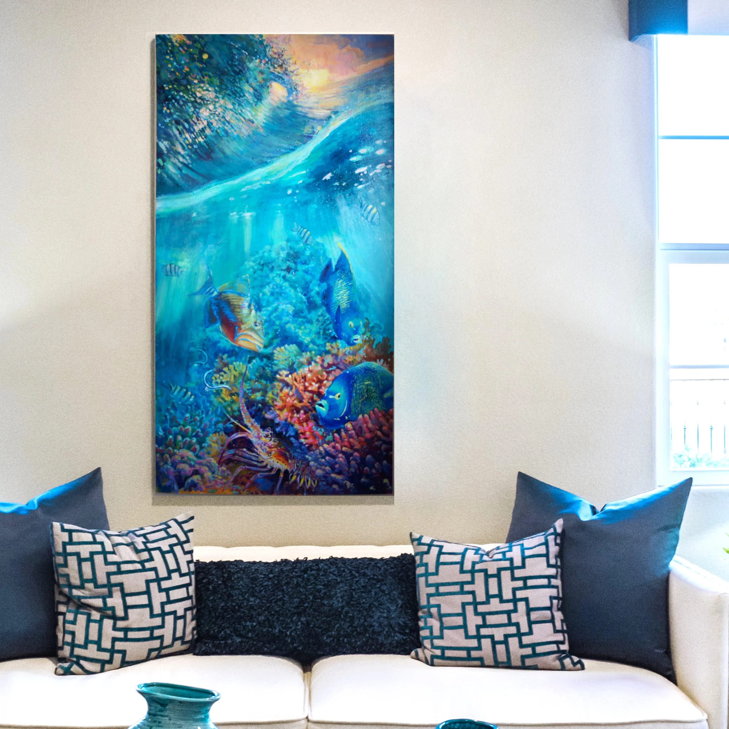 A living room with a white couch adorned with decorative pillows, a black pillow in the center, and patterned blue and white pillows on either side. A large, vibrant underwater-themed painting featuring colorful fish and coral is hung on the wall abo
