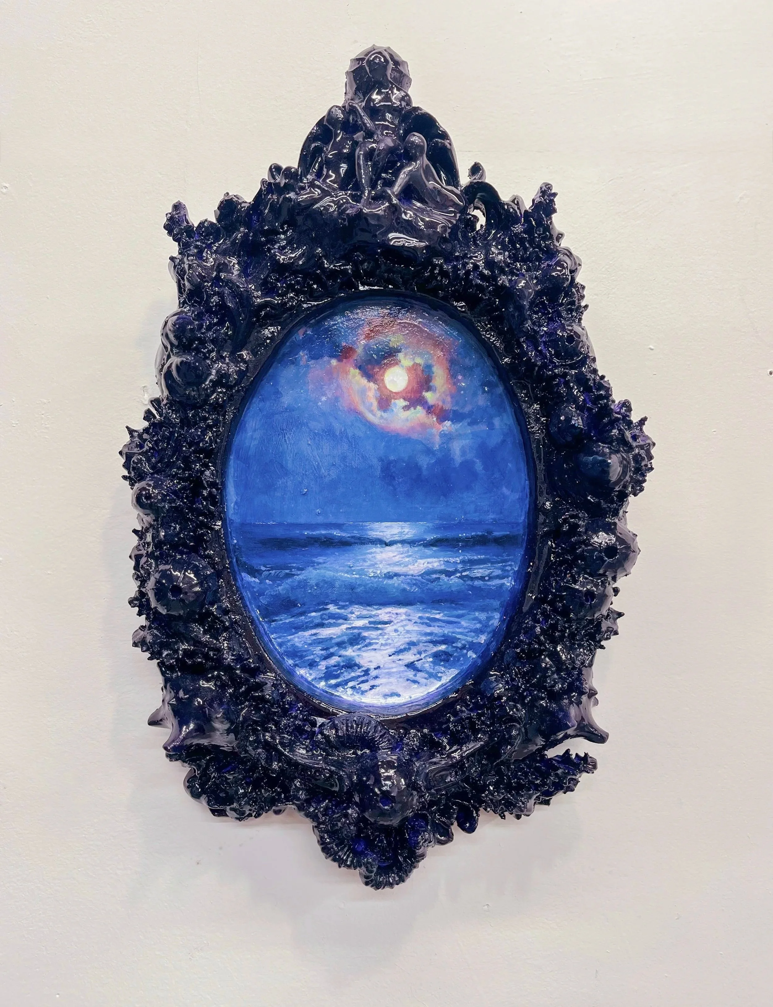 Framed artwork depicting a moonlit ocean scene with a rainbow-colored sky reflected on the water, surrounded by an ornate dark blue frame.