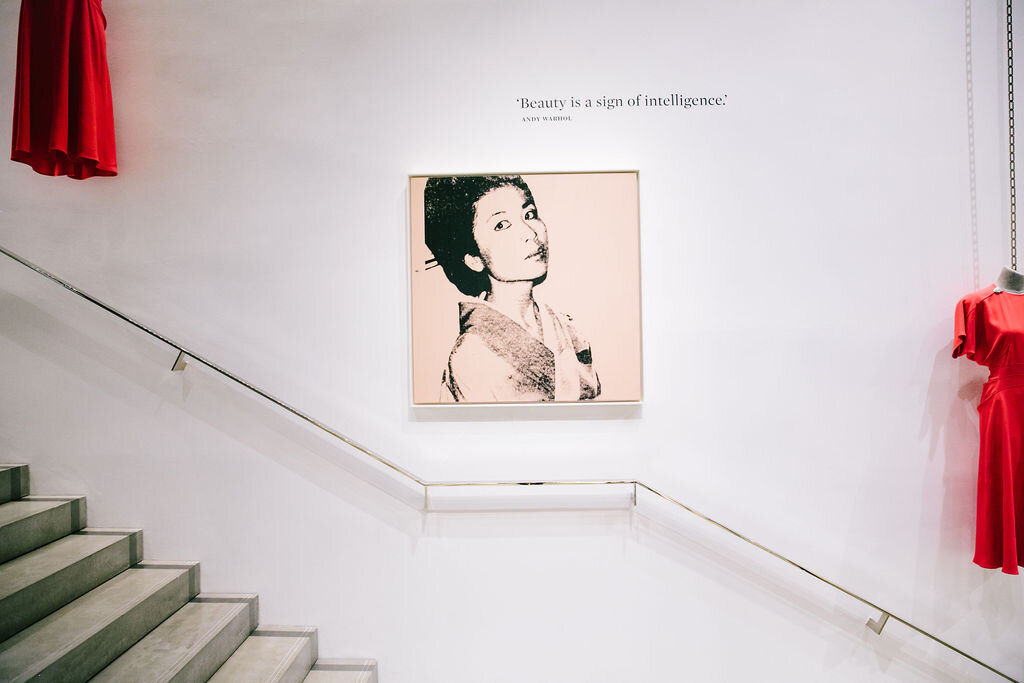 Warhol painting alongside two Victoria Beckham red dresses hung above a staircase