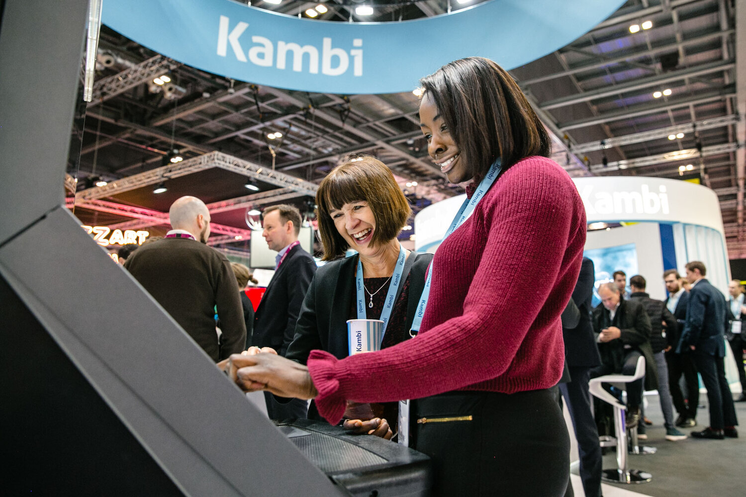 two women looking at a technology stand wearing lanyards smiling