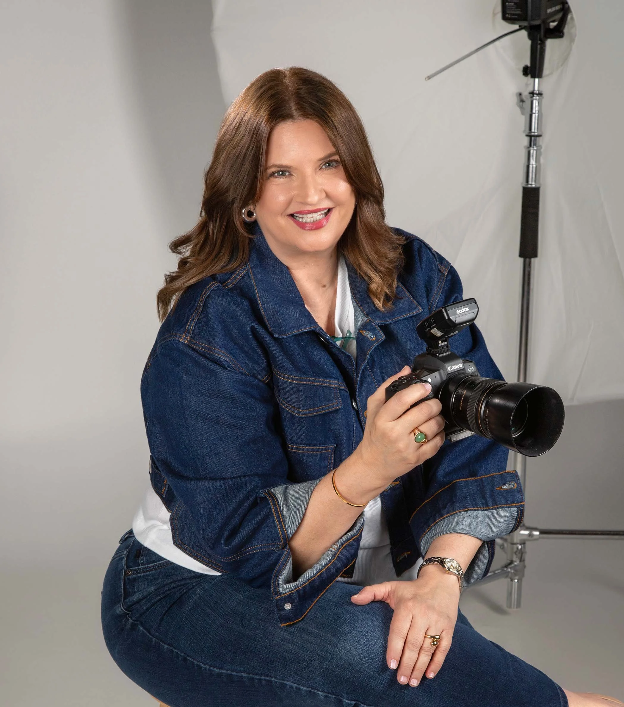Tulsa senior portrait photographer Jamil Gotcher smiling warmly at the camera and holding her Canon camera.