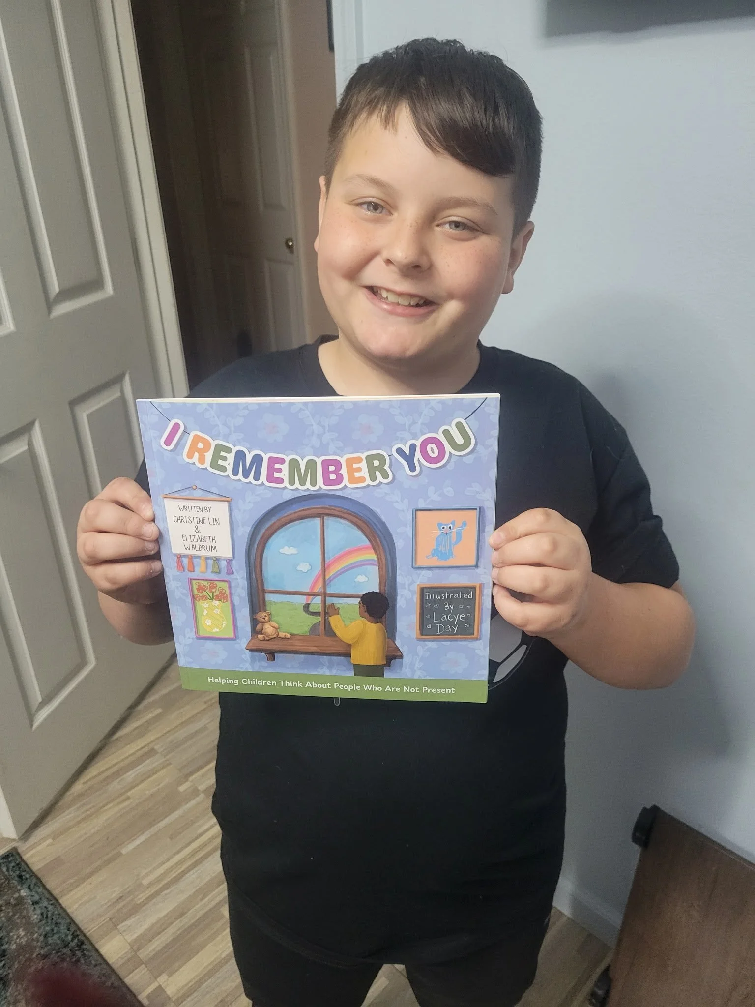 10 year old white boy with freckles and a big smile holds the book I Remember You