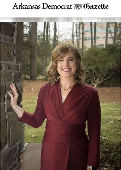 Woman with shoulder length brown hair and light skin stands next to a rock column smiling. She is wearing a maroon dress and fall leaves are in the background. Arkansas Democrat Gazette photo of Sarah Catherine Gutierrez