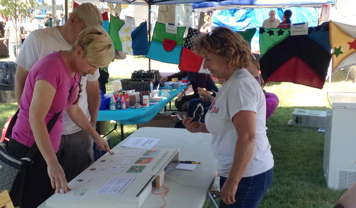 Local resident Julie Steuer mans the voting booth during Melon Days. Students flags on display in the background.
