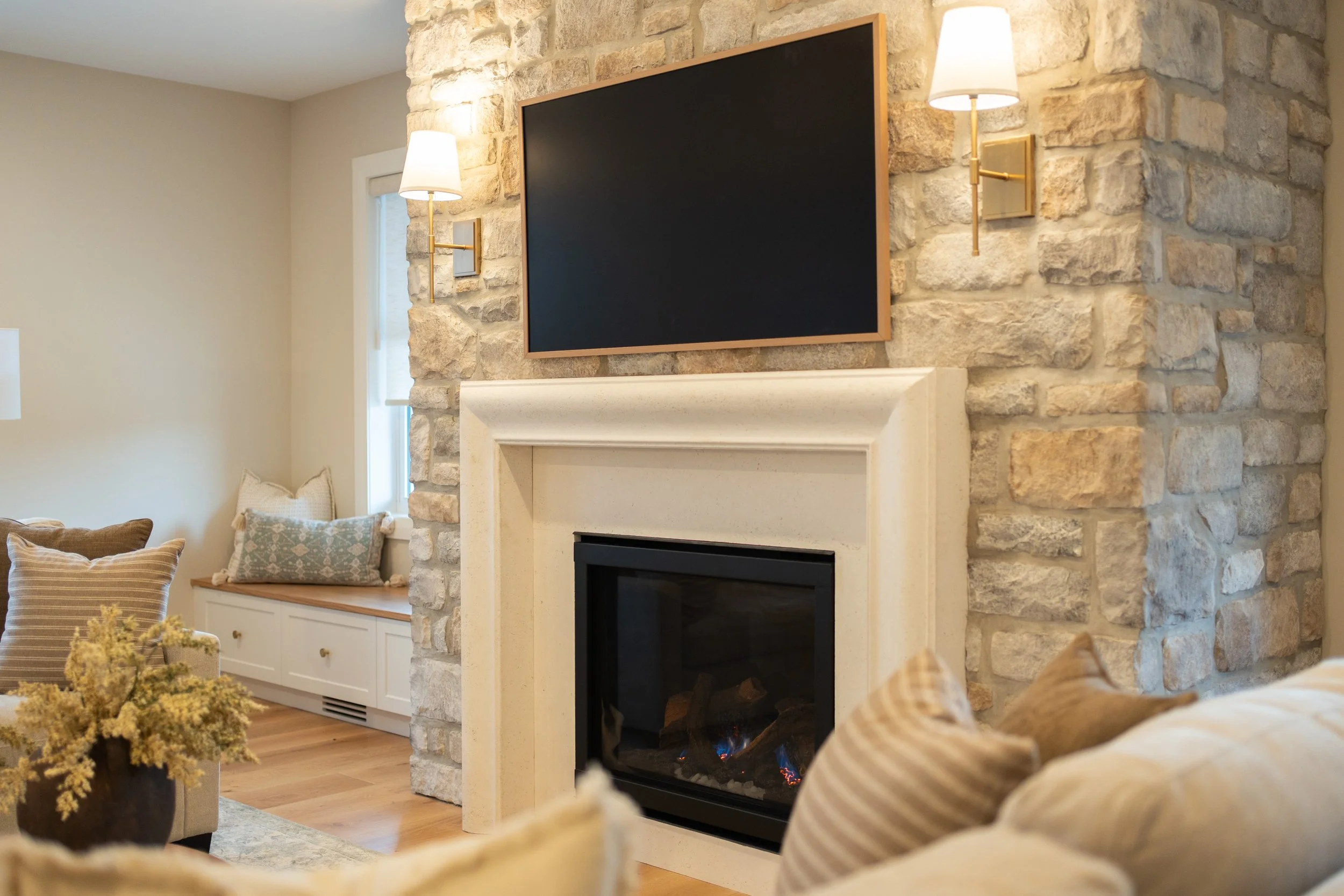 Angled view of a gas fireplace with a cast stone mantle, stone surround, and brass wall sconces