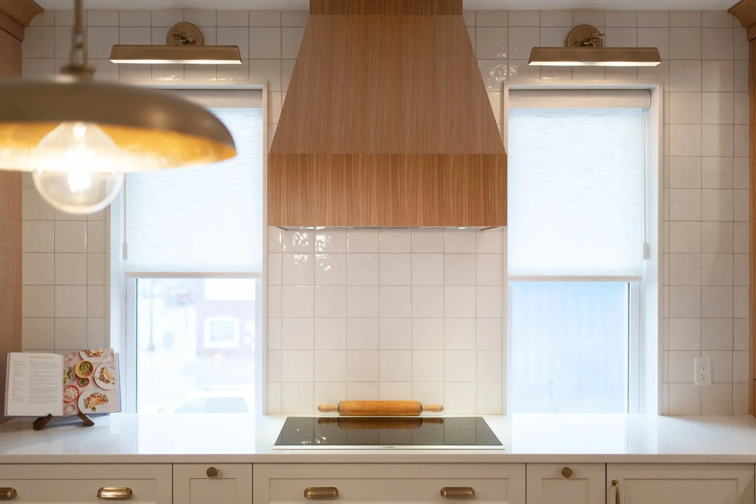 Kitchen with a wood range hood, white tile backsplash, and quartz countertops extending into the window sills