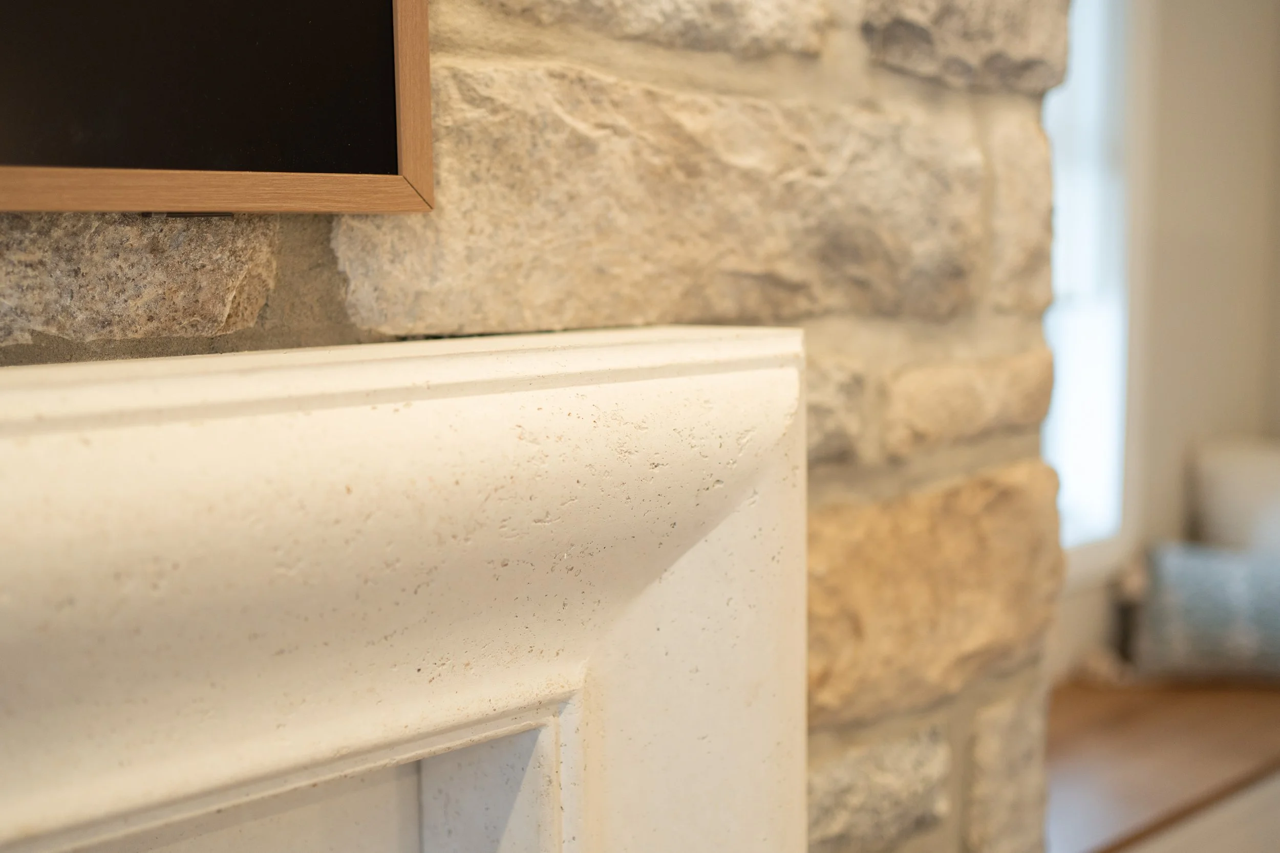 Close view of a fireplace with textured stone, custom mantle, and warm lighting from wall sconces