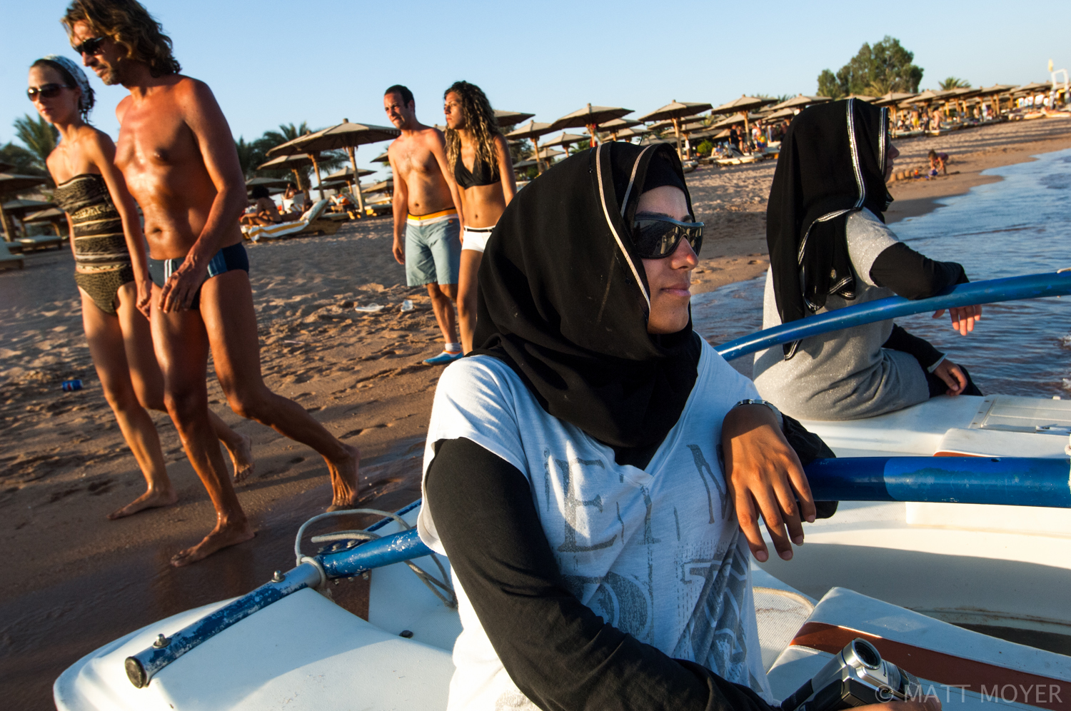  Two Jordanian sisters sit along the beach in Nama Bay, Egypt as European tourists stroll past in the Sinai. The Sinai is knows as a place where diverse cultures mix. 