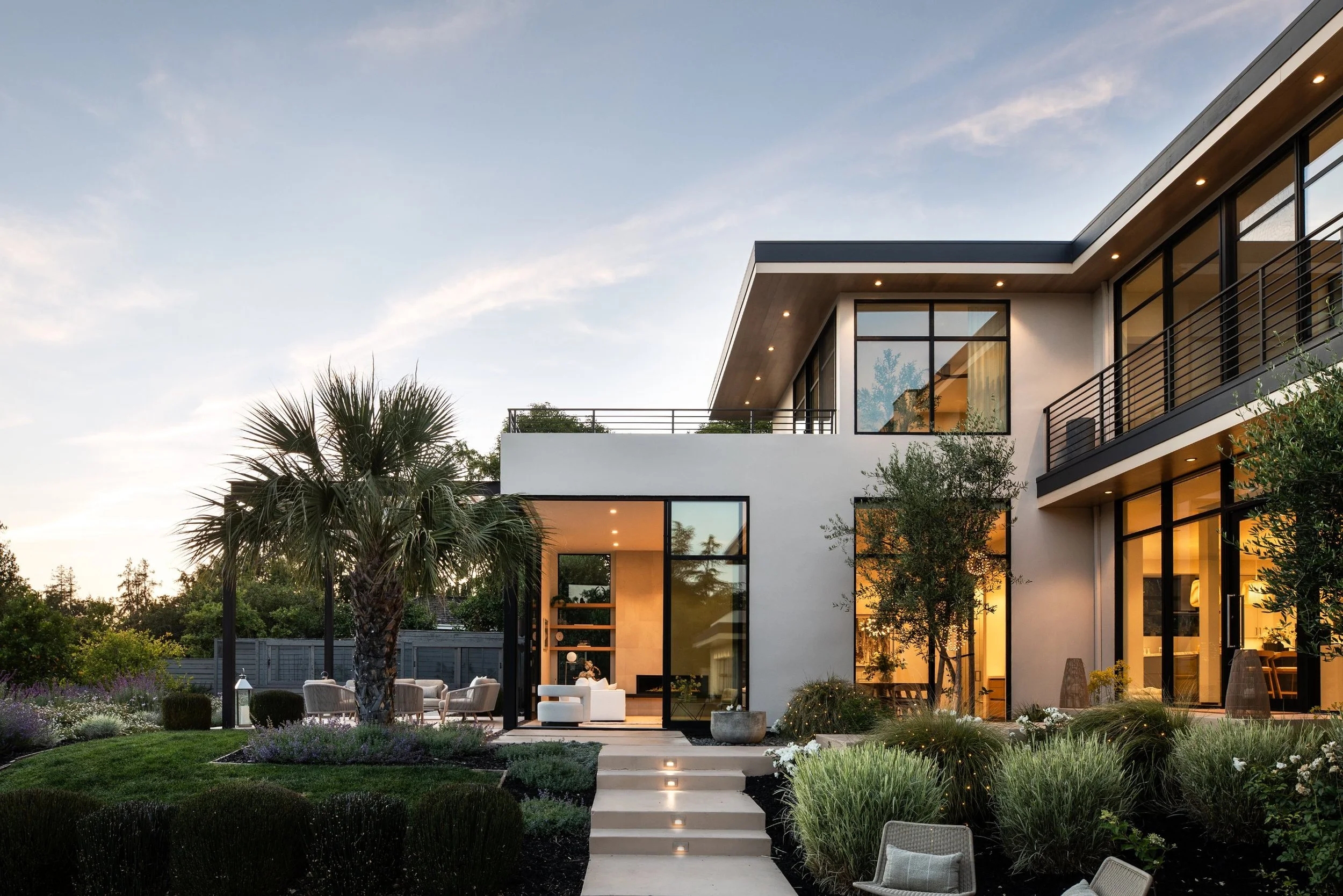 Entry courtyard at dusk with floor-to-ceiling glass and a lit outdoor living room, modern home in Los Altos, CA