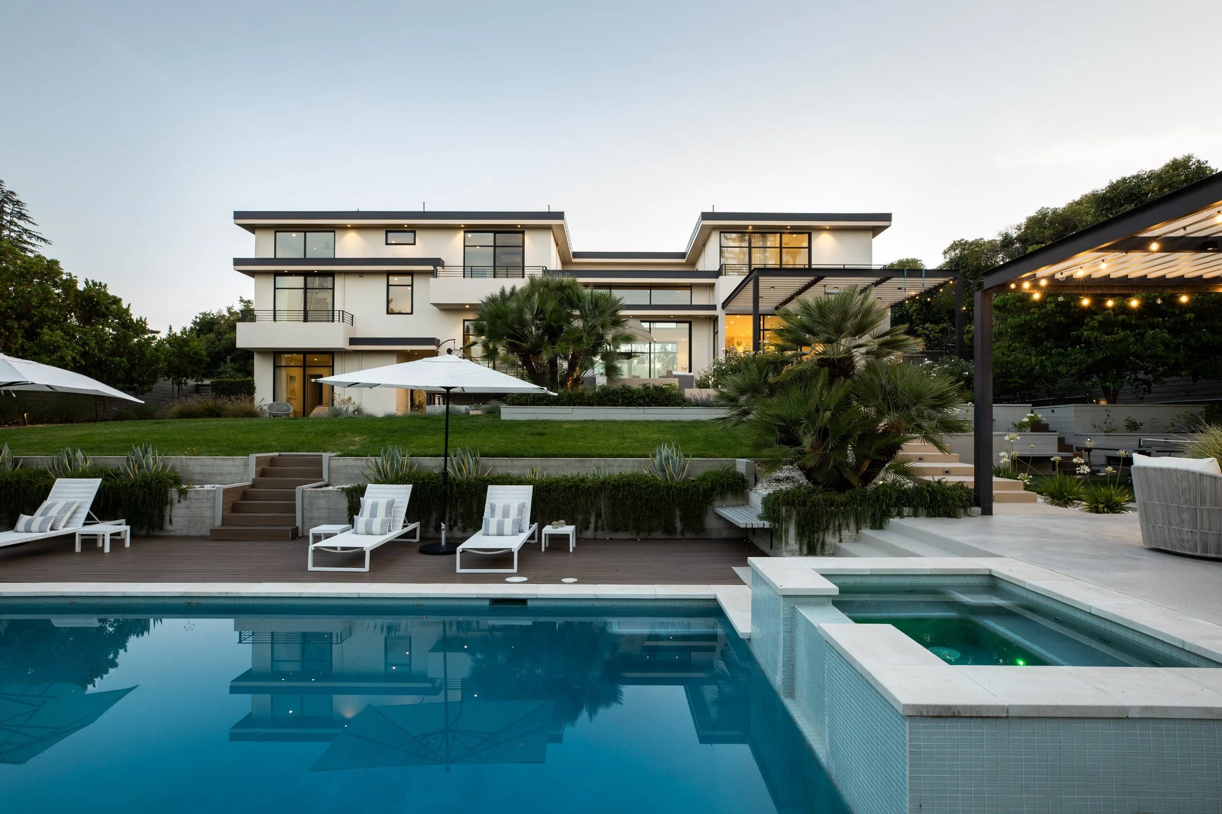 Rear facade of a three-story modern home across the pool and spa at dusk, Los Altos, CA