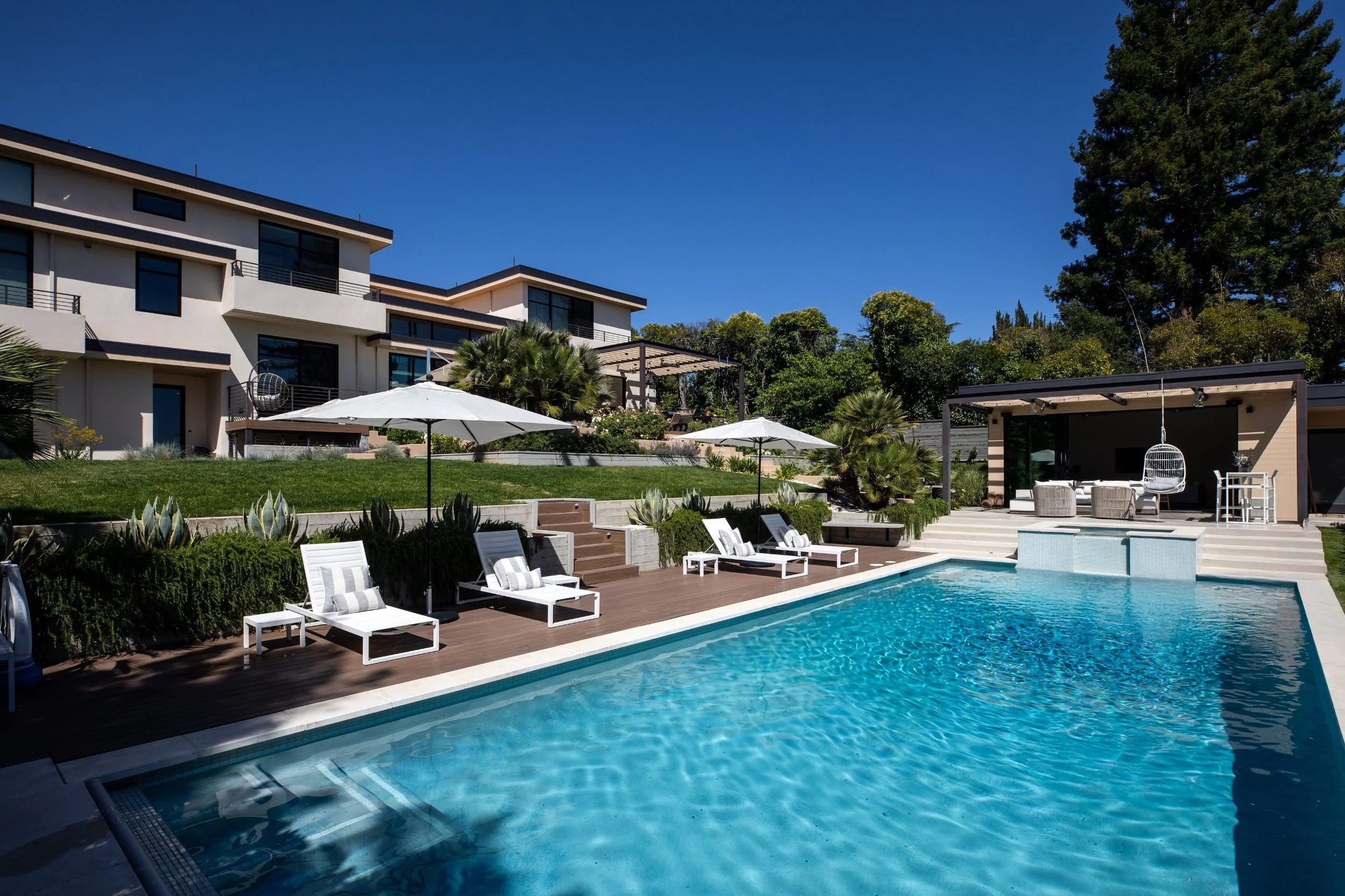 Pool, spa and pool house with a pergola behind a modern custom home in Los Altos, CA