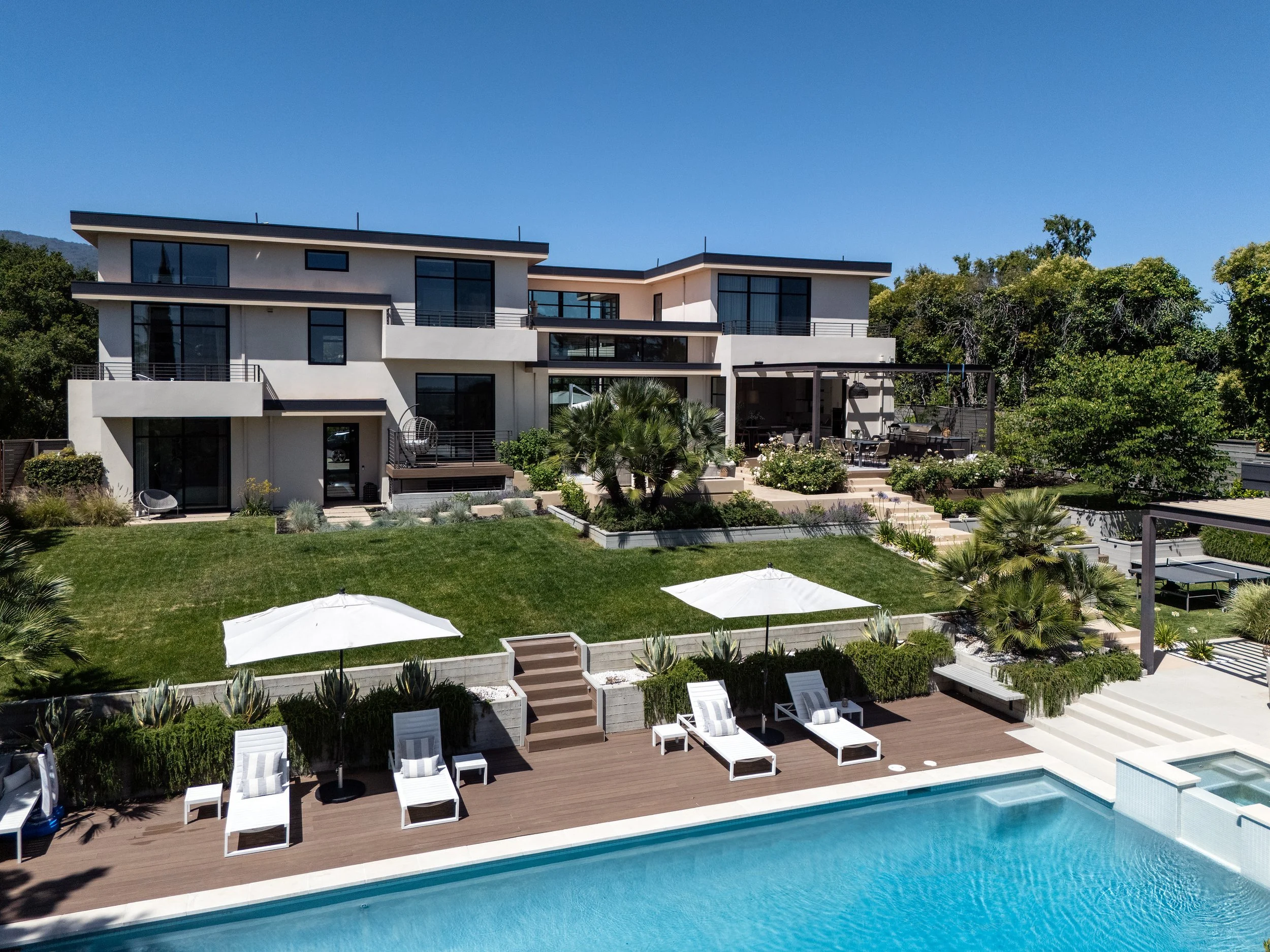 Aerial view of the rear terraces, lawn and pool deck of a modern residence in Los Altos, CA