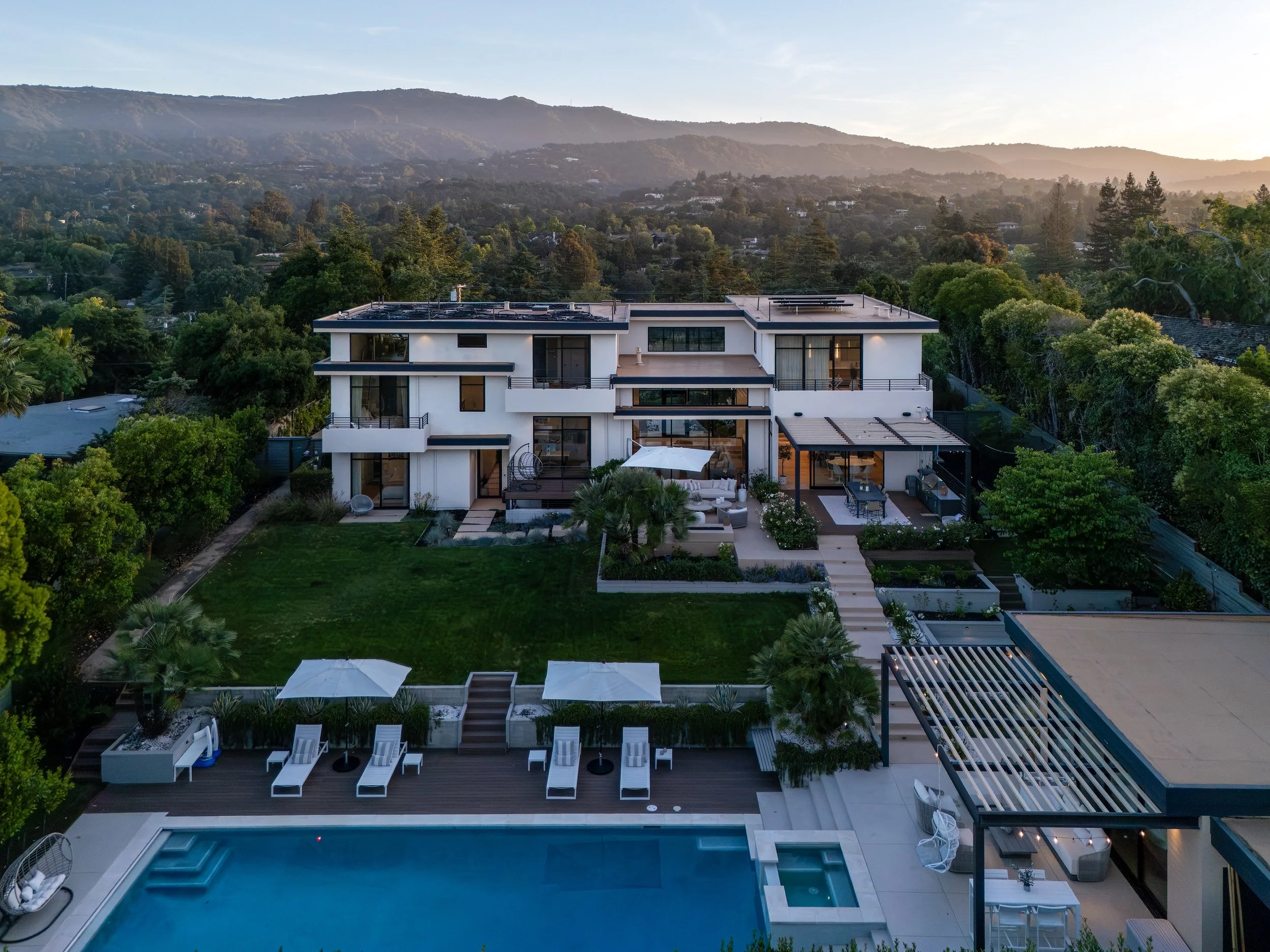 Aerial view at sunset of a modern Los Altos, CA home and pool against the Santa Cruz Mountains