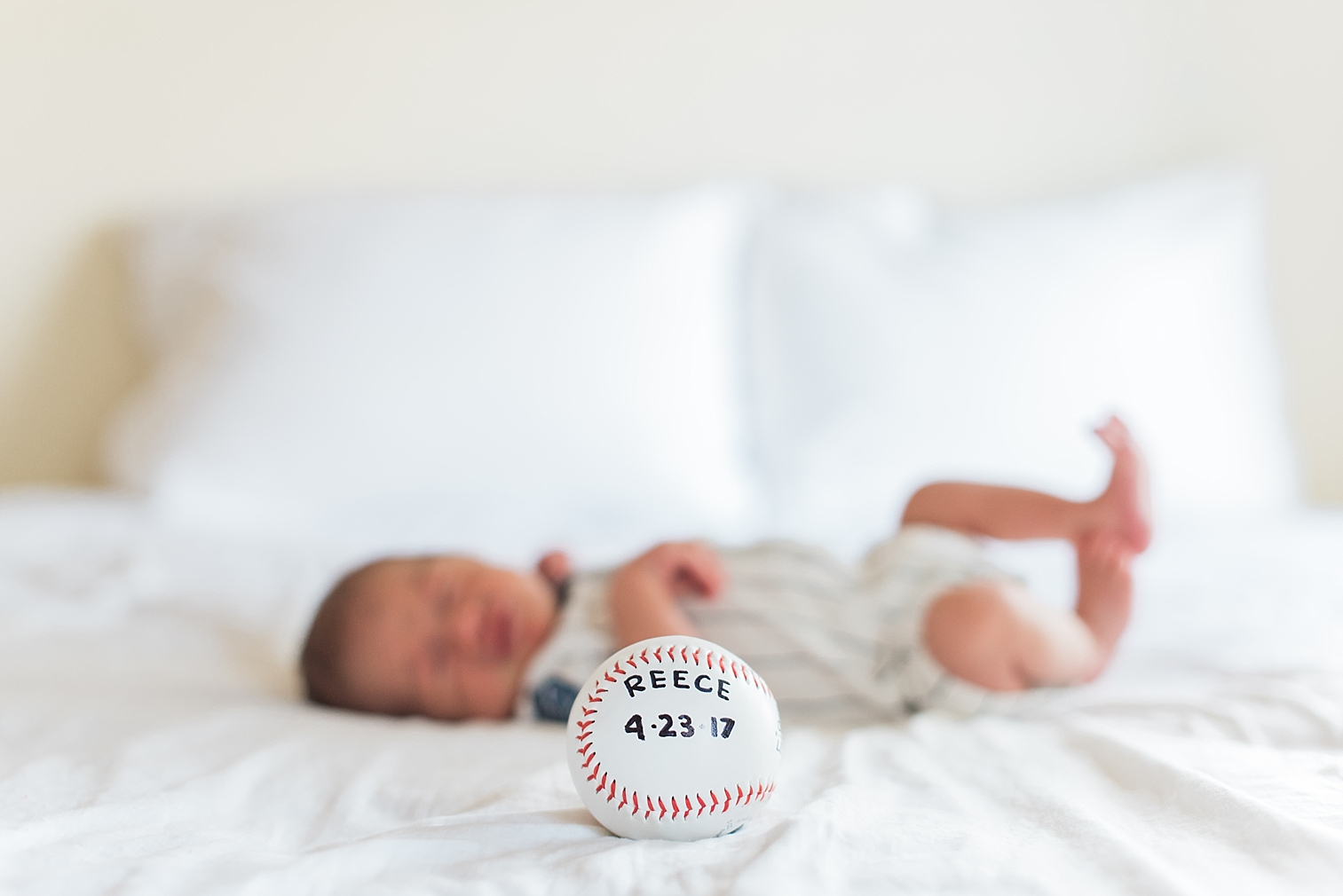 baby boy lays on bed with a baseball