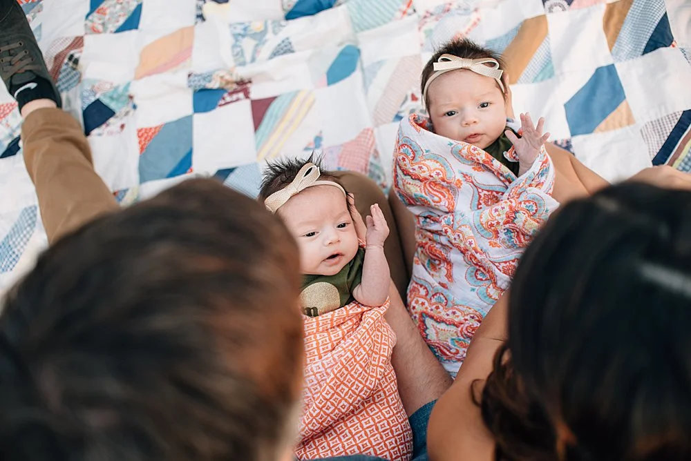 a photography of twin girls being held by their parents looking from above