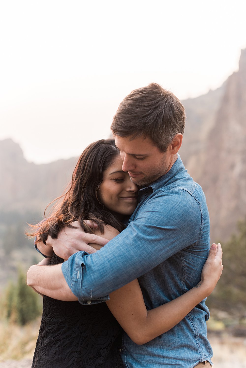  A husband and wife lovingly hug each other with Smith Rock, Oregon as a backdrop. 