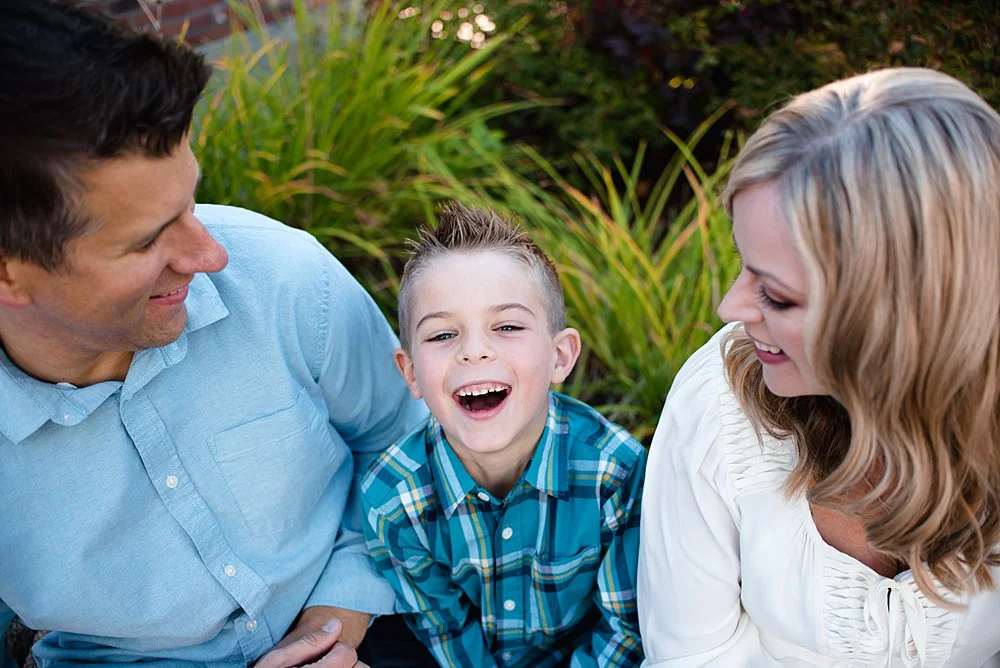 a boy looks up at the camera laughing while his mom and dad tickle him