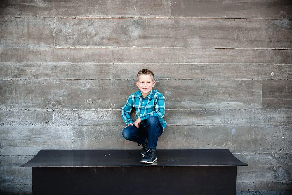 Boy poses while squatting on a bench in front of the shops at the Old Mill District in Bend Oregon