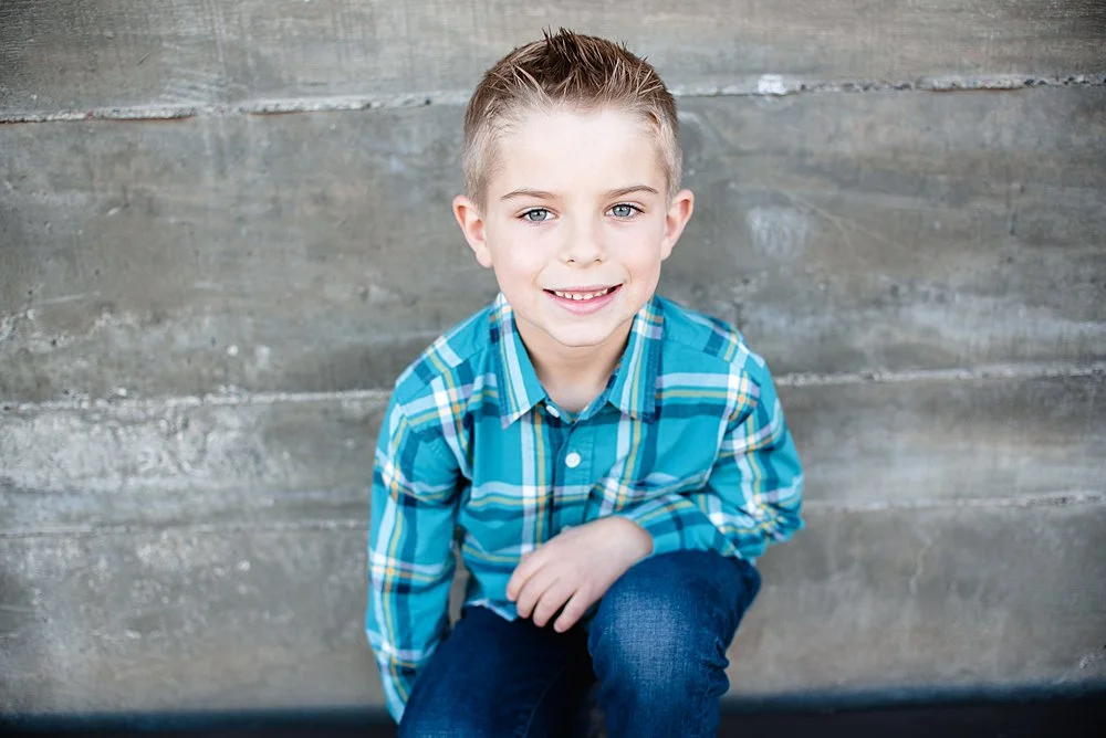 a close up of a boy posing in front of a stone wall smiling at the camera in Bend Oregon