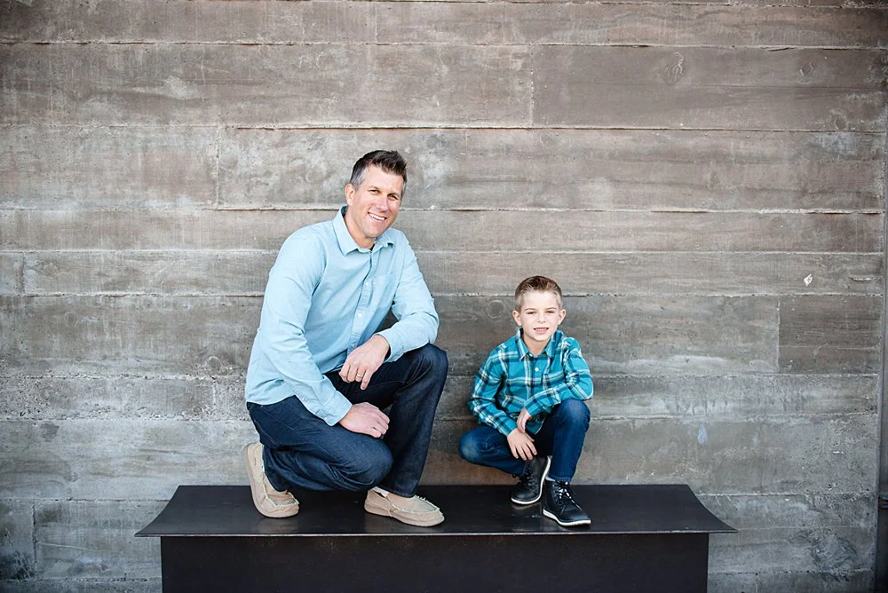 A boy and his dad pose on a bench in front of a stone wall in Bend Oregon