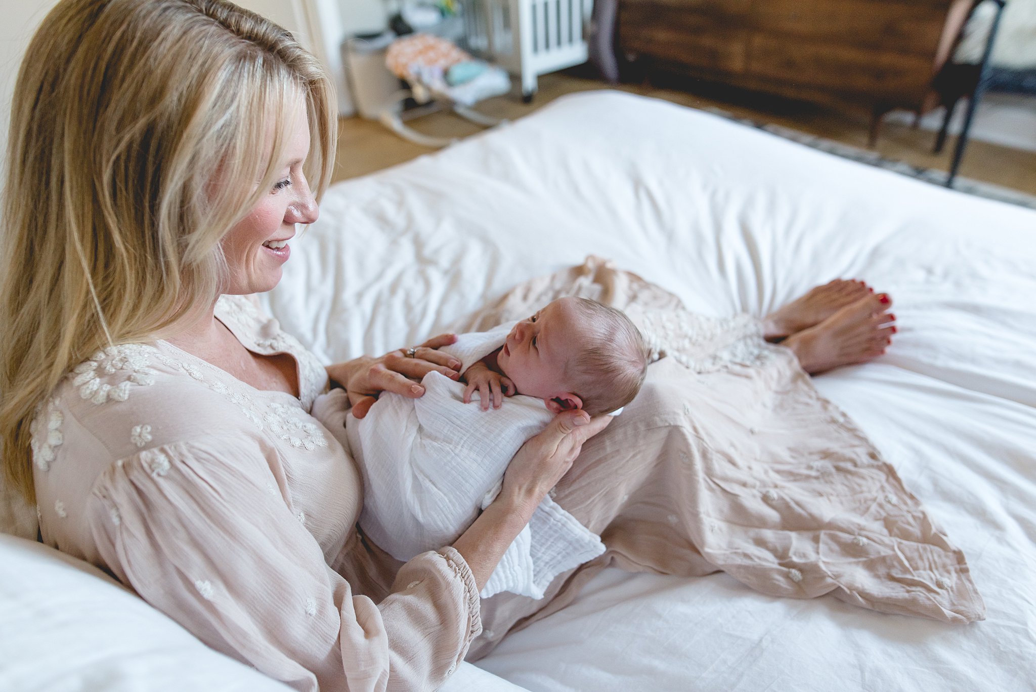  mom sits on bed with her newborn baby girl. 