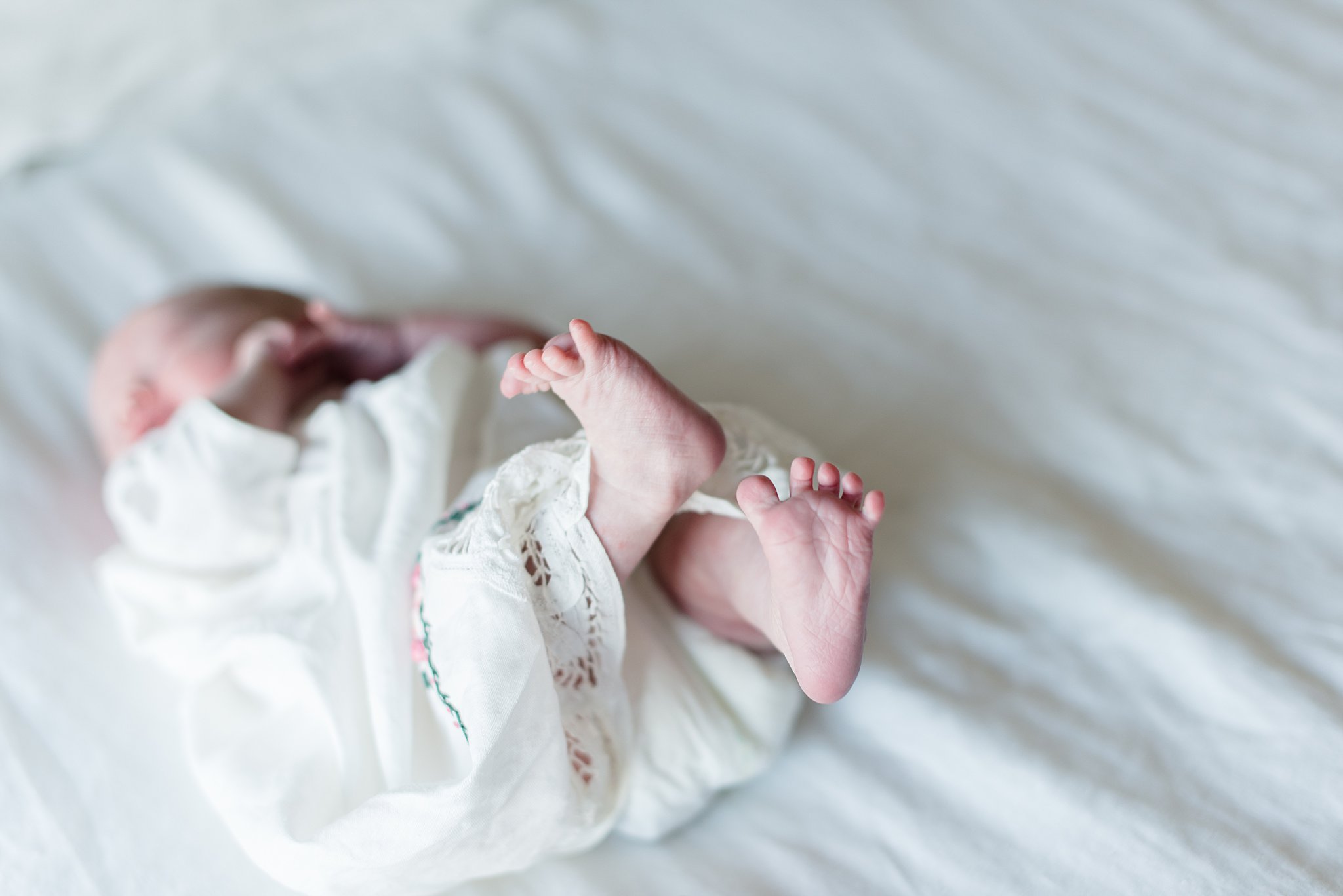  little baby lies on bed with her tiny feet in the air 