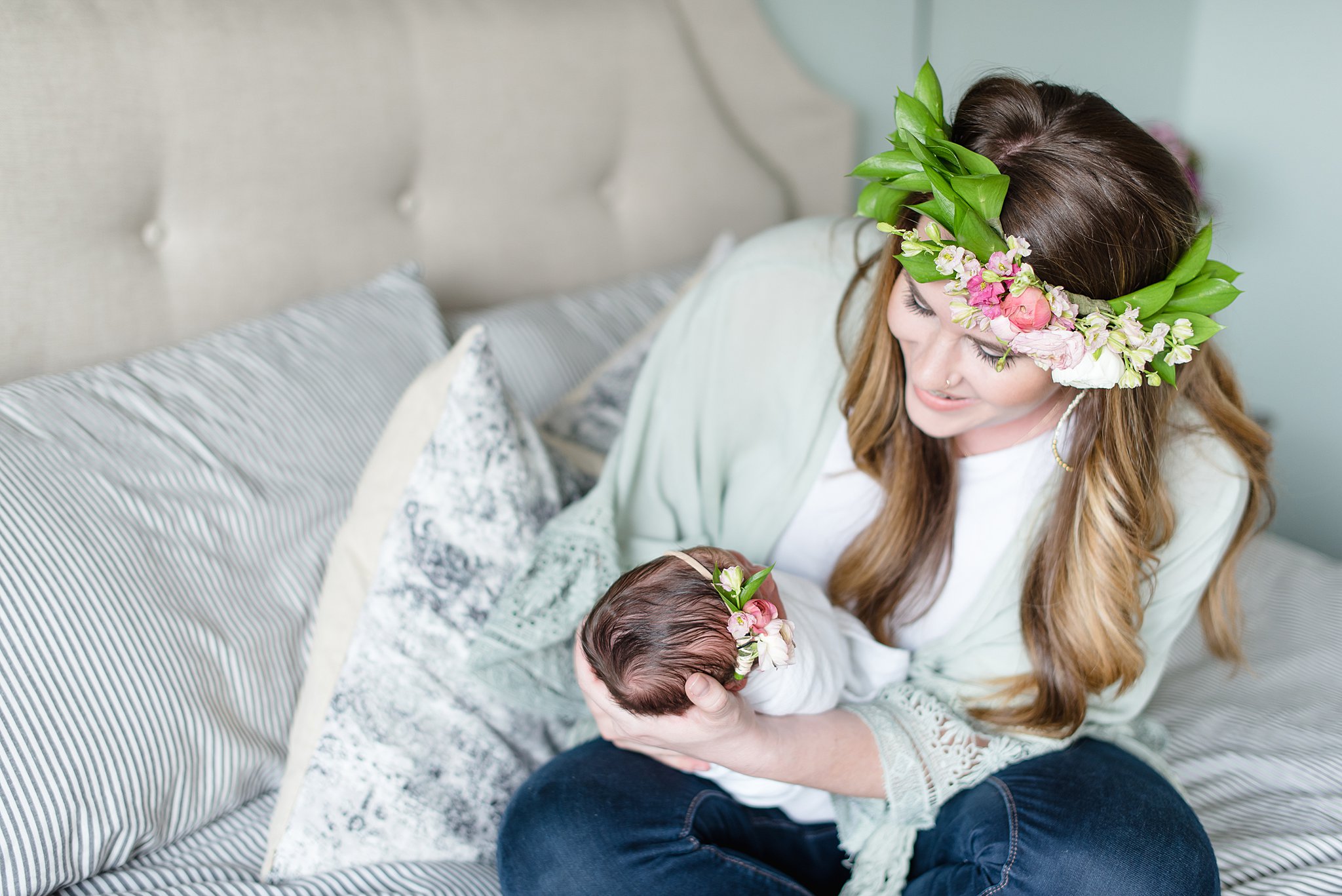  a mother wearing a flower crown smiles at her new baby  