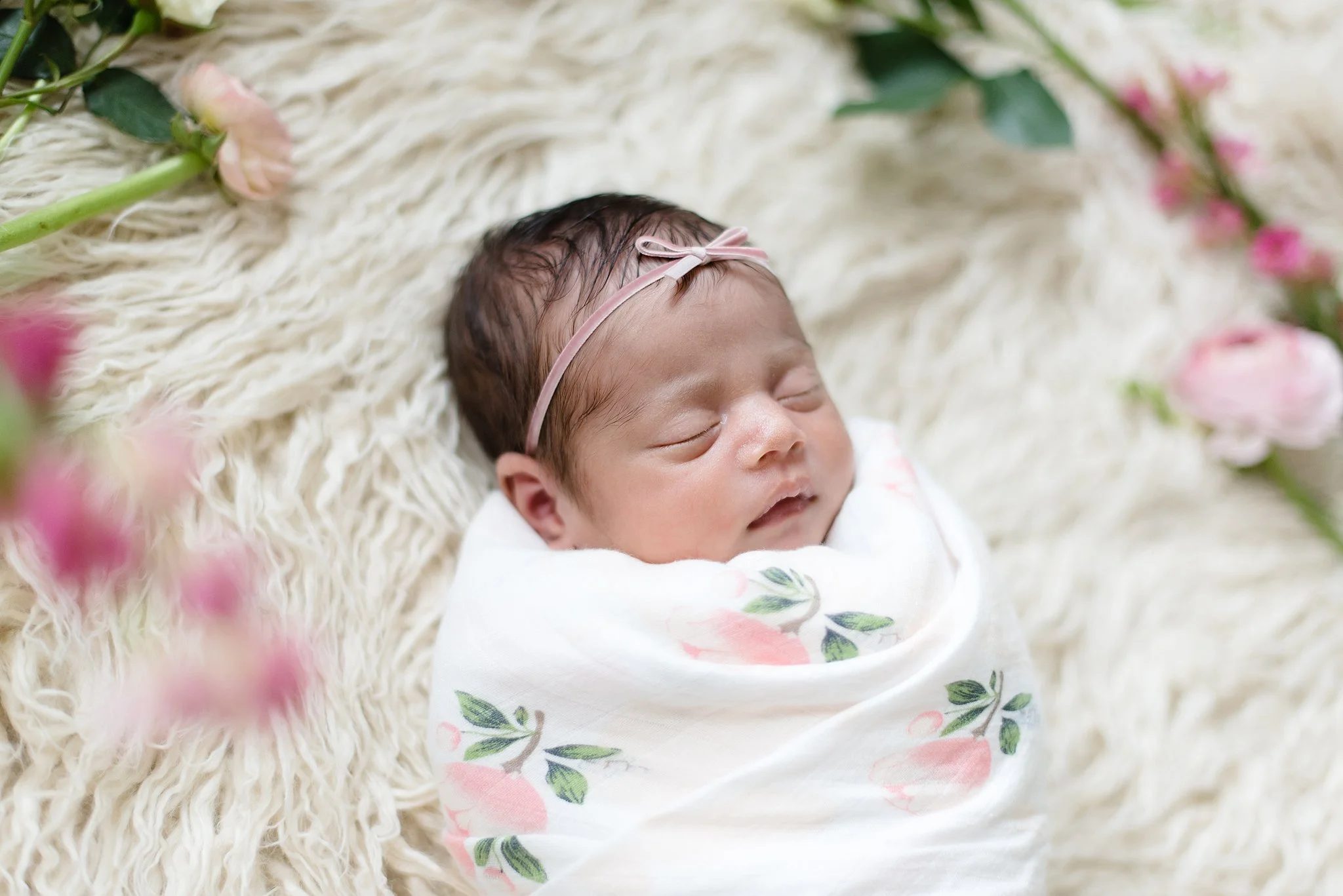 a portrait of a baby girl swaddled and wearing a bow