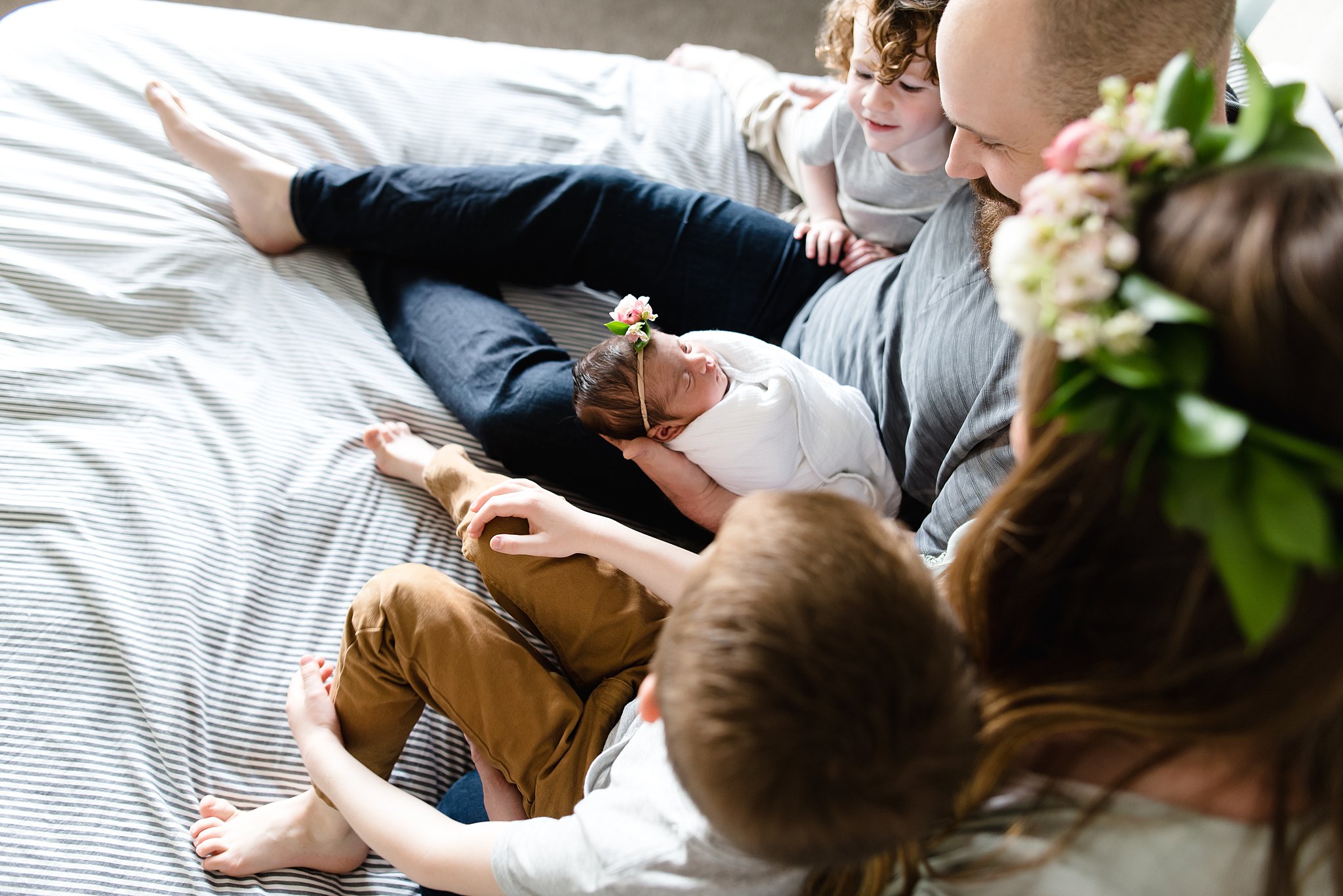  family is cozy together on a bed gazing adoringly at their new baby girl 