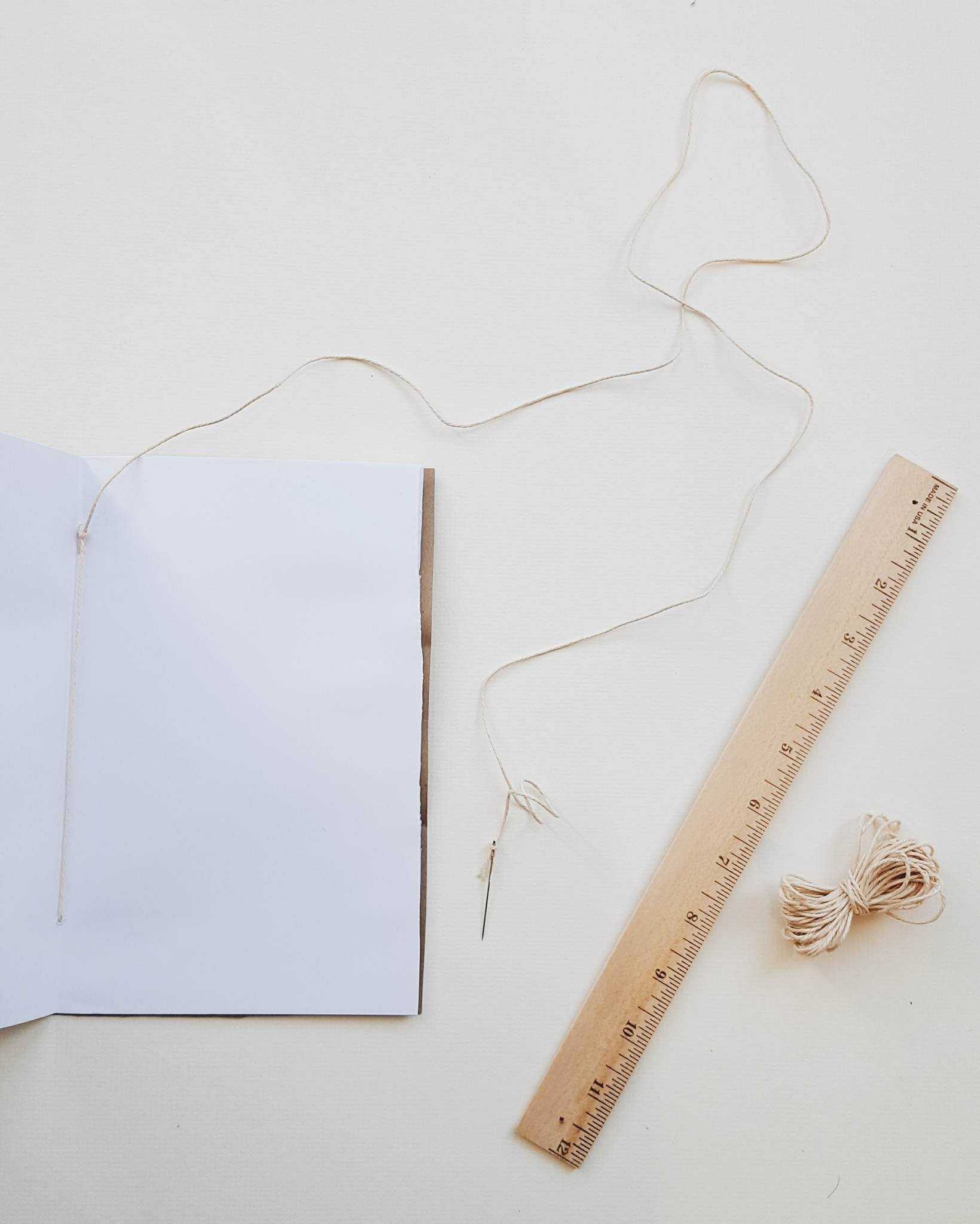 Time to bind your journal together! Take around 10 sheets of office paper + your newly cut kraft cover and fold in half. On your fold line, mark two spots two inches from the outsides. These will be your stitching marks! Staring from the inside, puncture a hole going outward with your needle & thread and then return the thread through the opposing hole. Tie together with a tight little not (pictures above.)