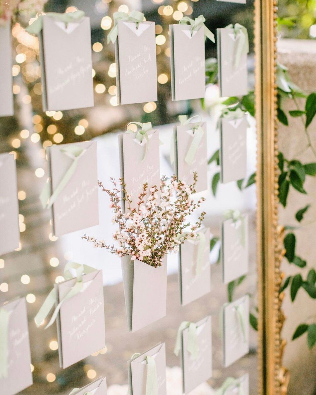 Loved this escort wall featuring raw silk ribbon and vellum table number overlays all on a gorgeous gold mirror with pops of floral interspersed!