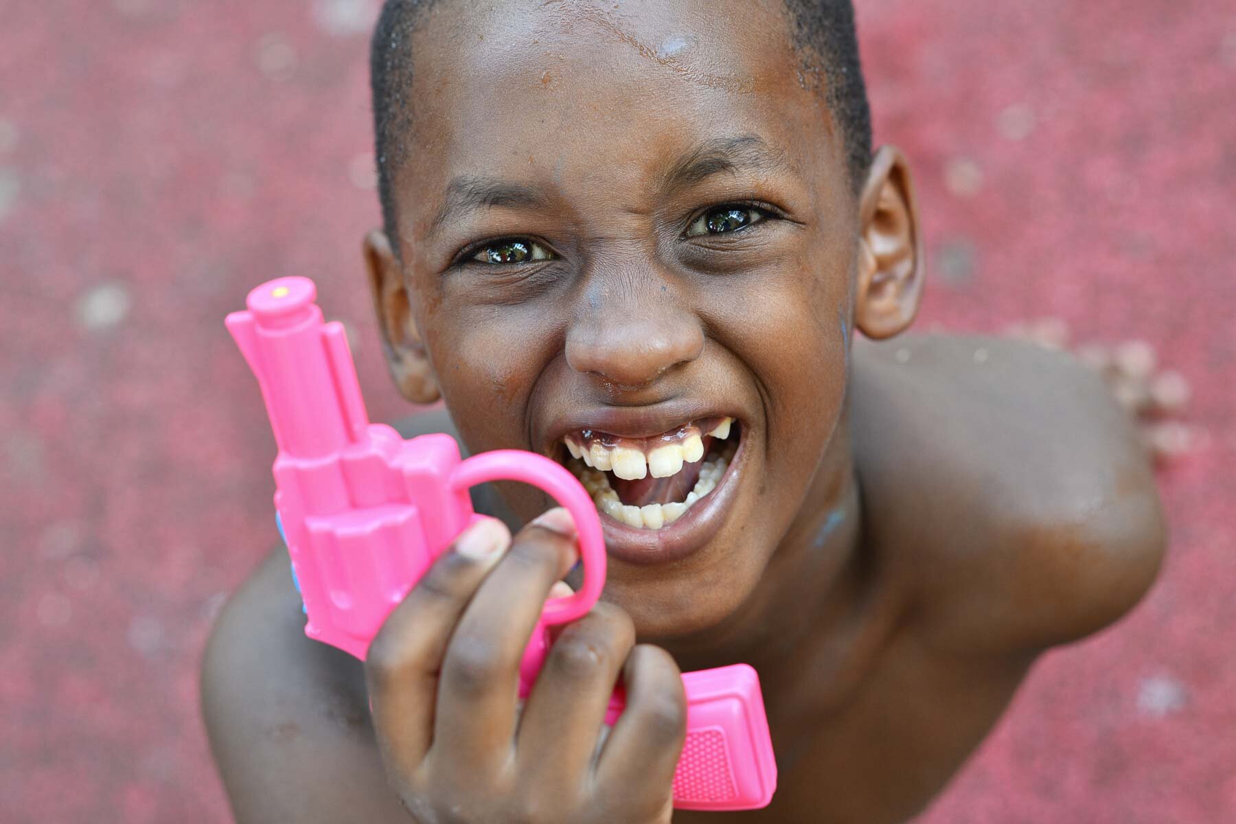  A young boy playing with a pink water-pistol. 