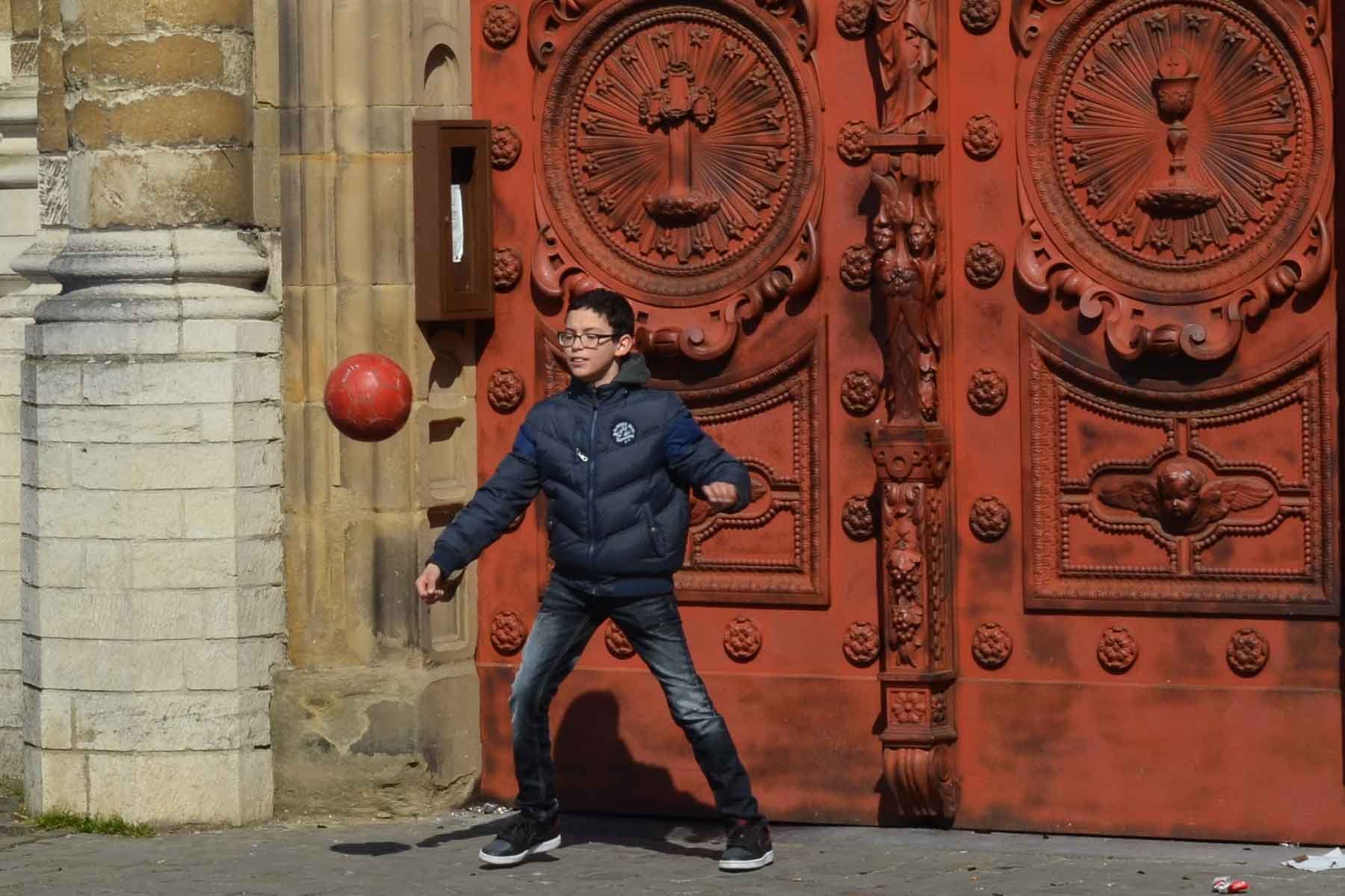  Boy playing with a ball in front of the Église Saint-Jean-Baptiste au Béguinage. 