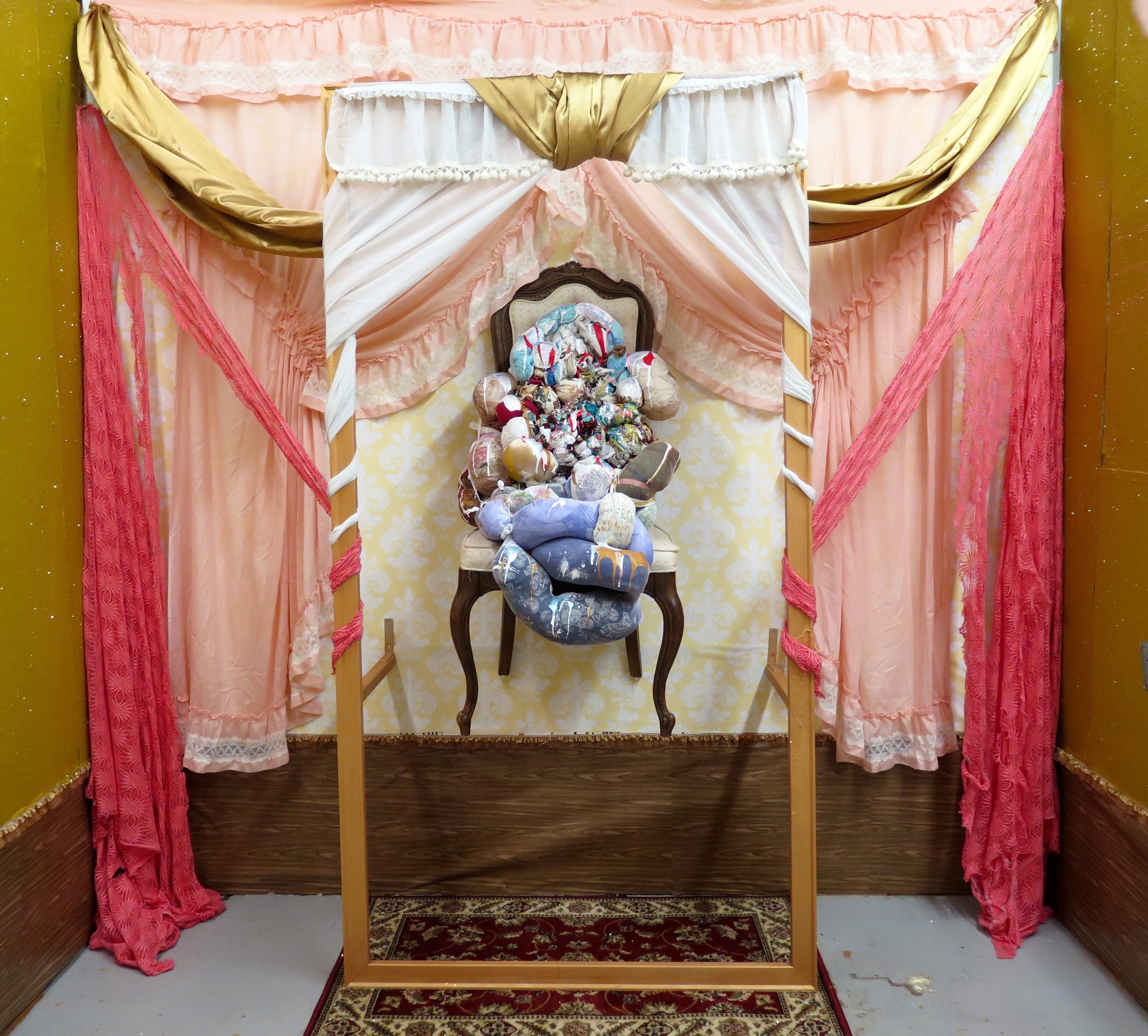  2016,  Mother Mary   Studio installation. Repurposed chair,  Hang In There  sculpture, synthetic silk fabric, lace, repurposed curtains, 88"x44" stretcher bar frame, faux-wood adhesive contact paper, frilly lace trim, damask contact wallpaper, "baby