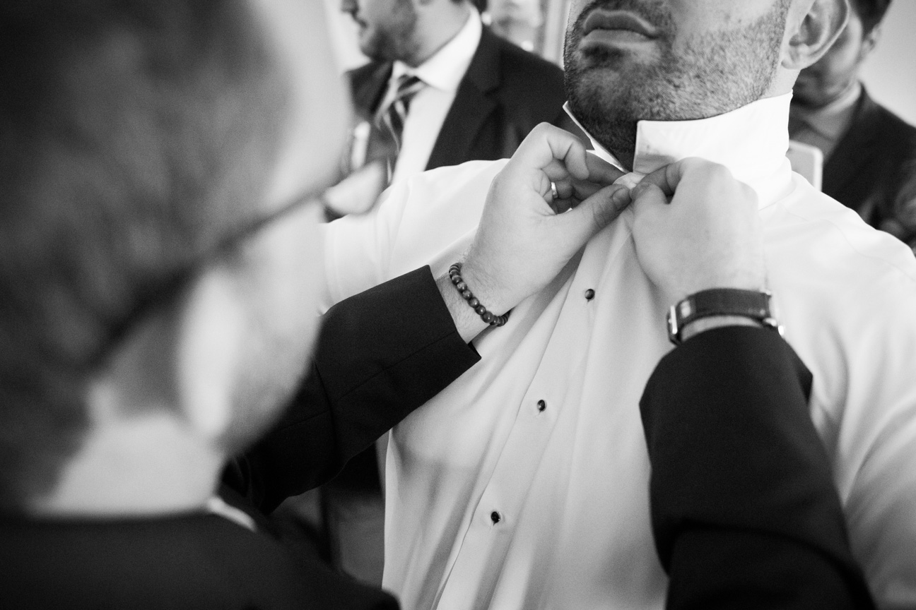 Groomsman helping the Groom button his shirt