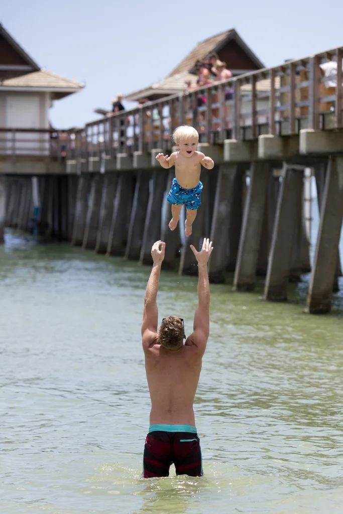  18-month-old Logan McGuire is thrown in the air by his dad Gabin McGuire by the Naples Pier on June 20, 2016. 