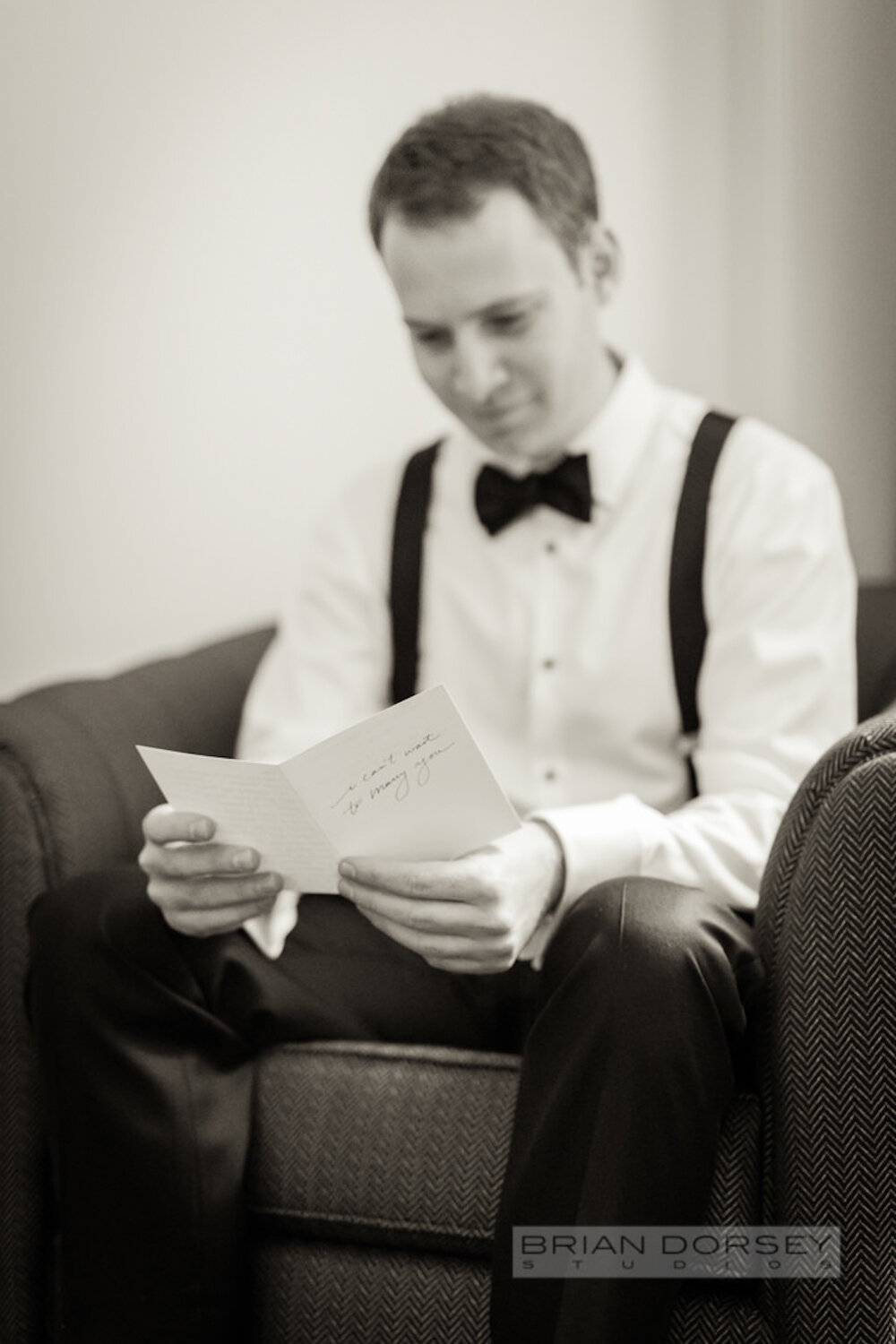 Groom in black tie reading a card on his wedding day