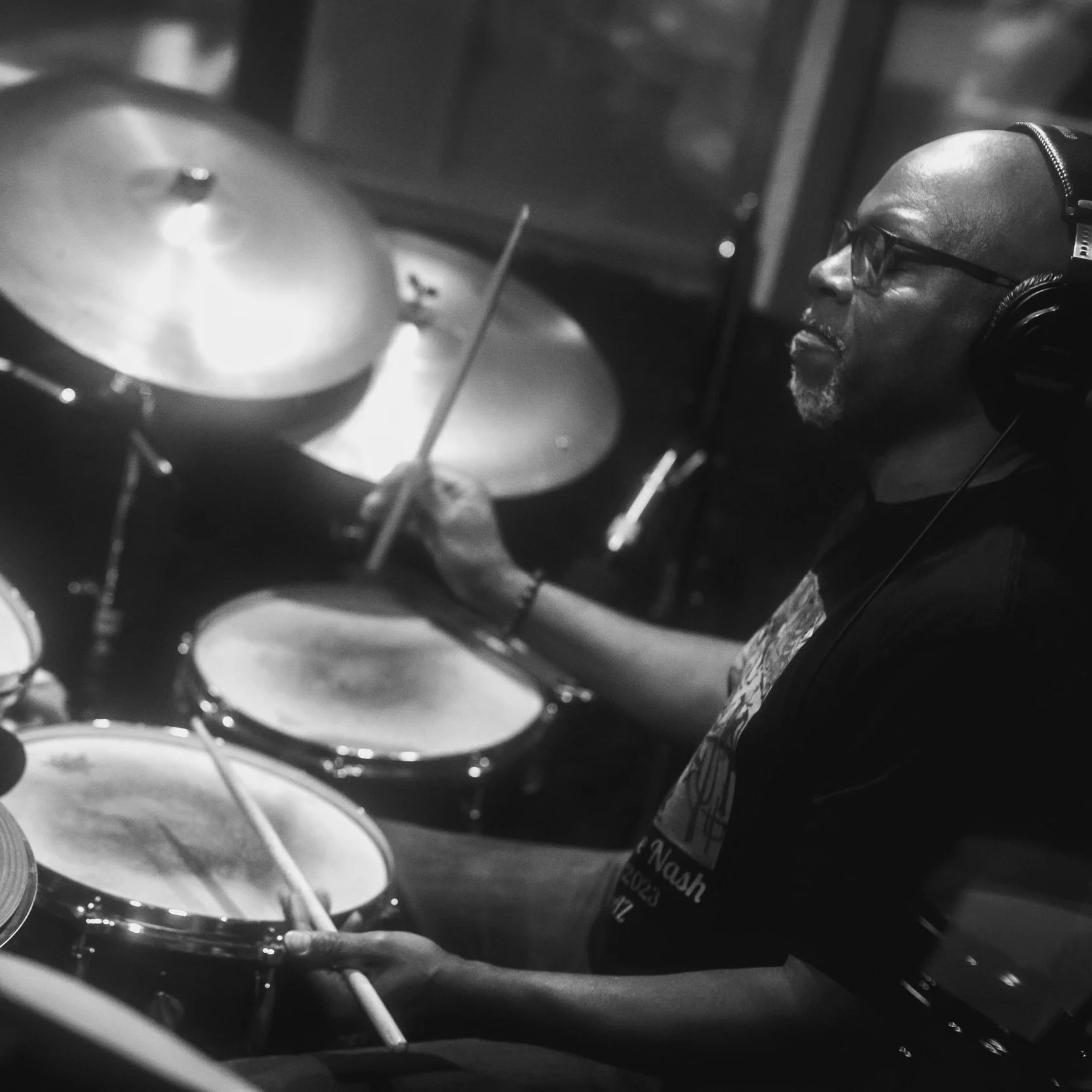 A man wearing headphones and glasses playing drums in a recording studio. Lewis Nash, drummer