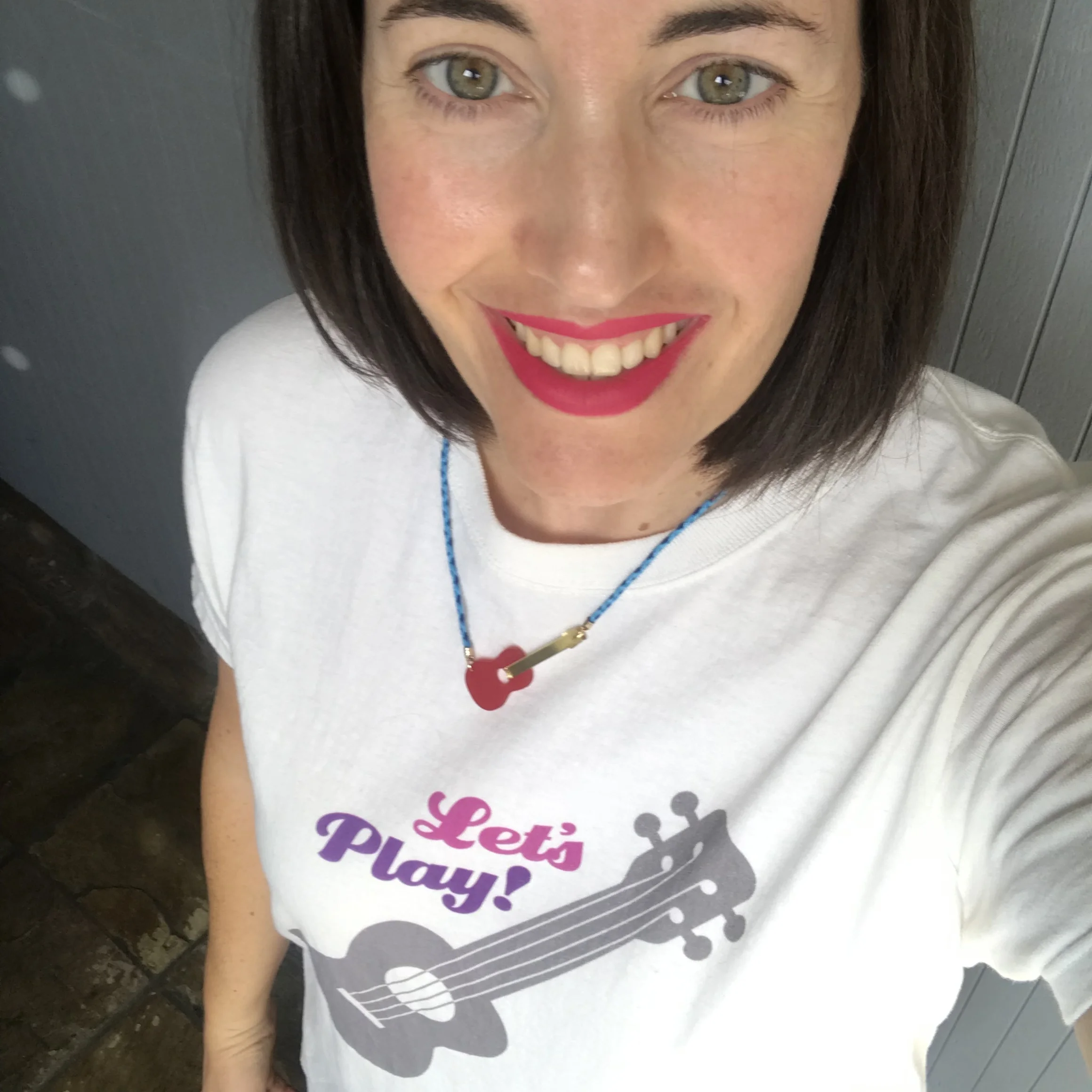 Wearing the new merch: an adorable ukulele necklace and a Let’s Play t-shirt.