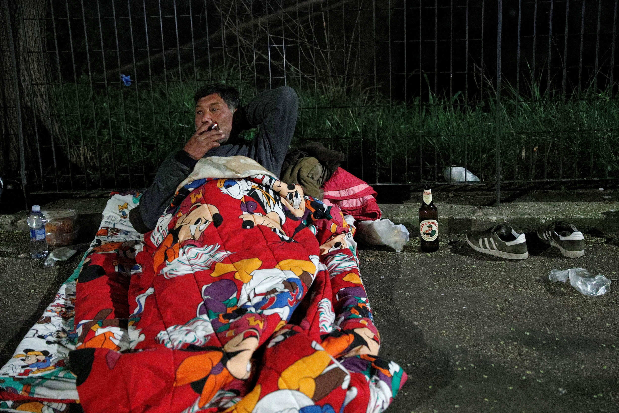  A homeless person smokes a cigarette as he lies on a pavement in Rome, Italy, March 17, 2020. Since the coronavirus crisis, Red Cross workers have been increasing their daily activities to meet the growing needs of the homeless in Rome.  