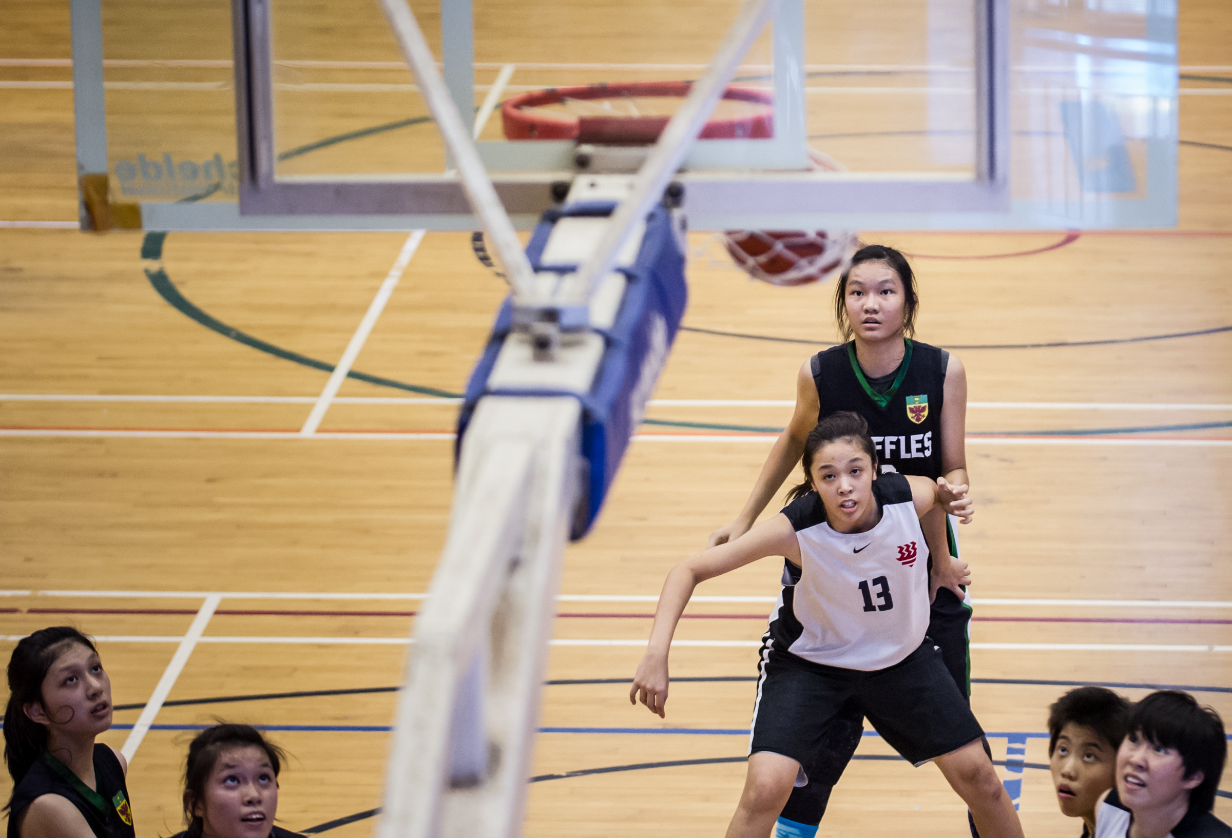 Basketball players watch as the ball makes the basket during a National Schools match at the Jurong East Sports Complex.